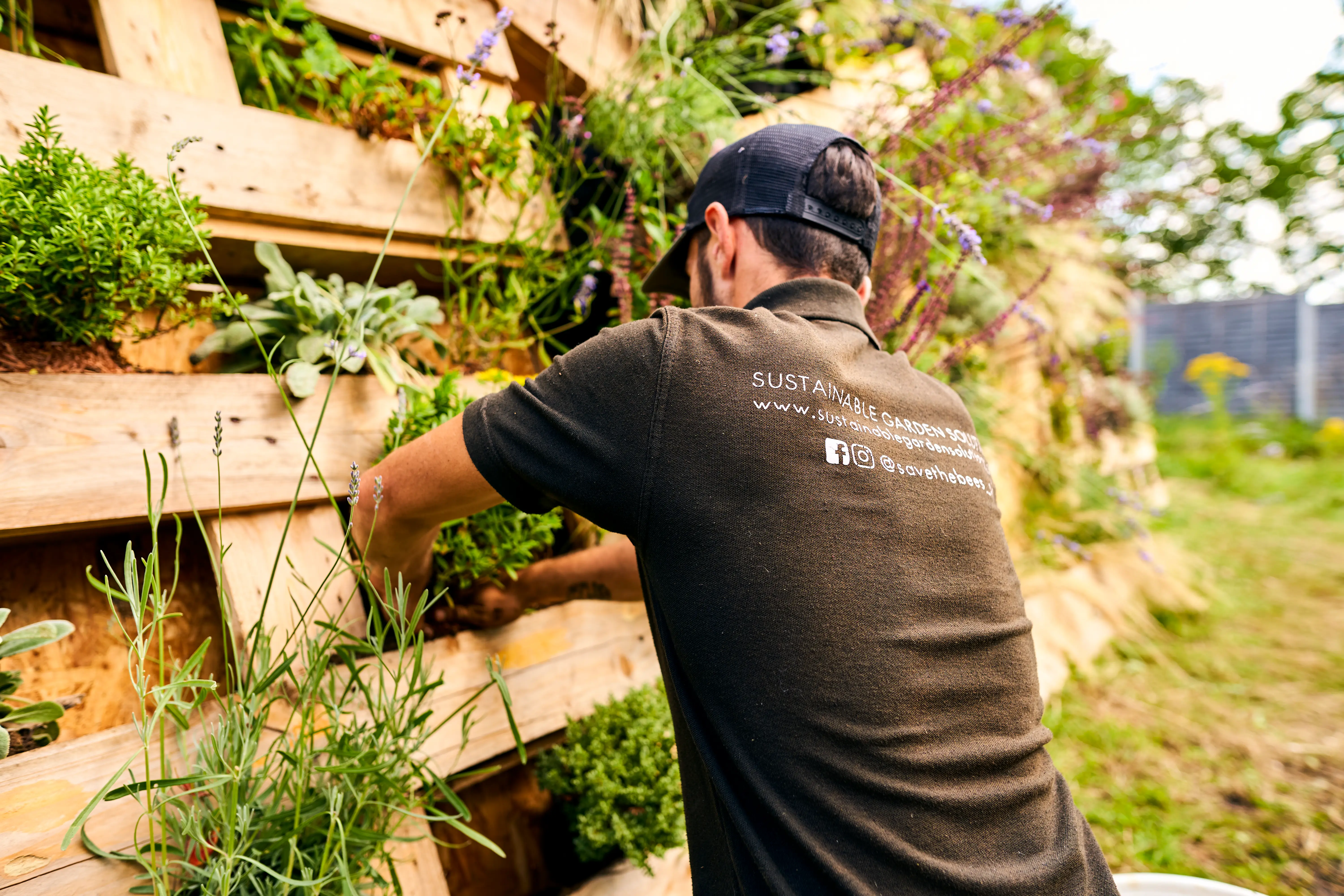 A person tends to a vertical garden made of wood pallets, surrounded by greenery.