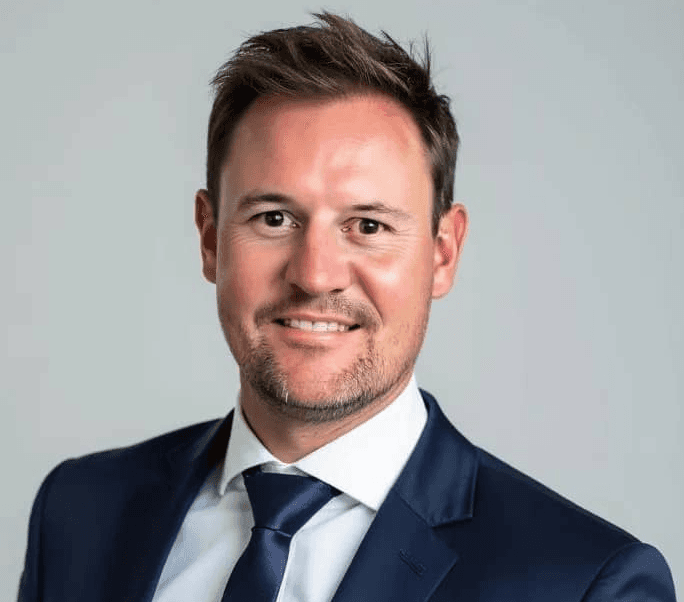 A woman with short curly hair wearing a black t-shirt looks into the camera.