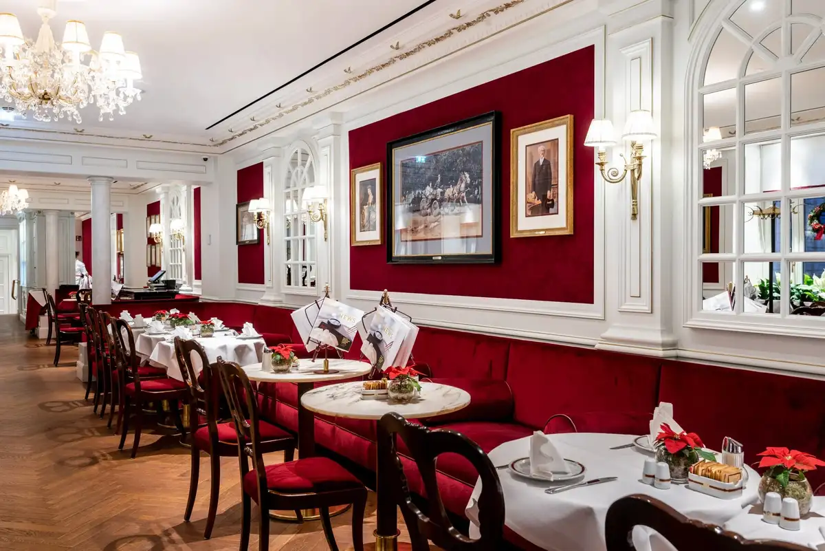 An elegant restaurant interior with red walls, white wainscoting, chandeliers, and tables set with white linens and