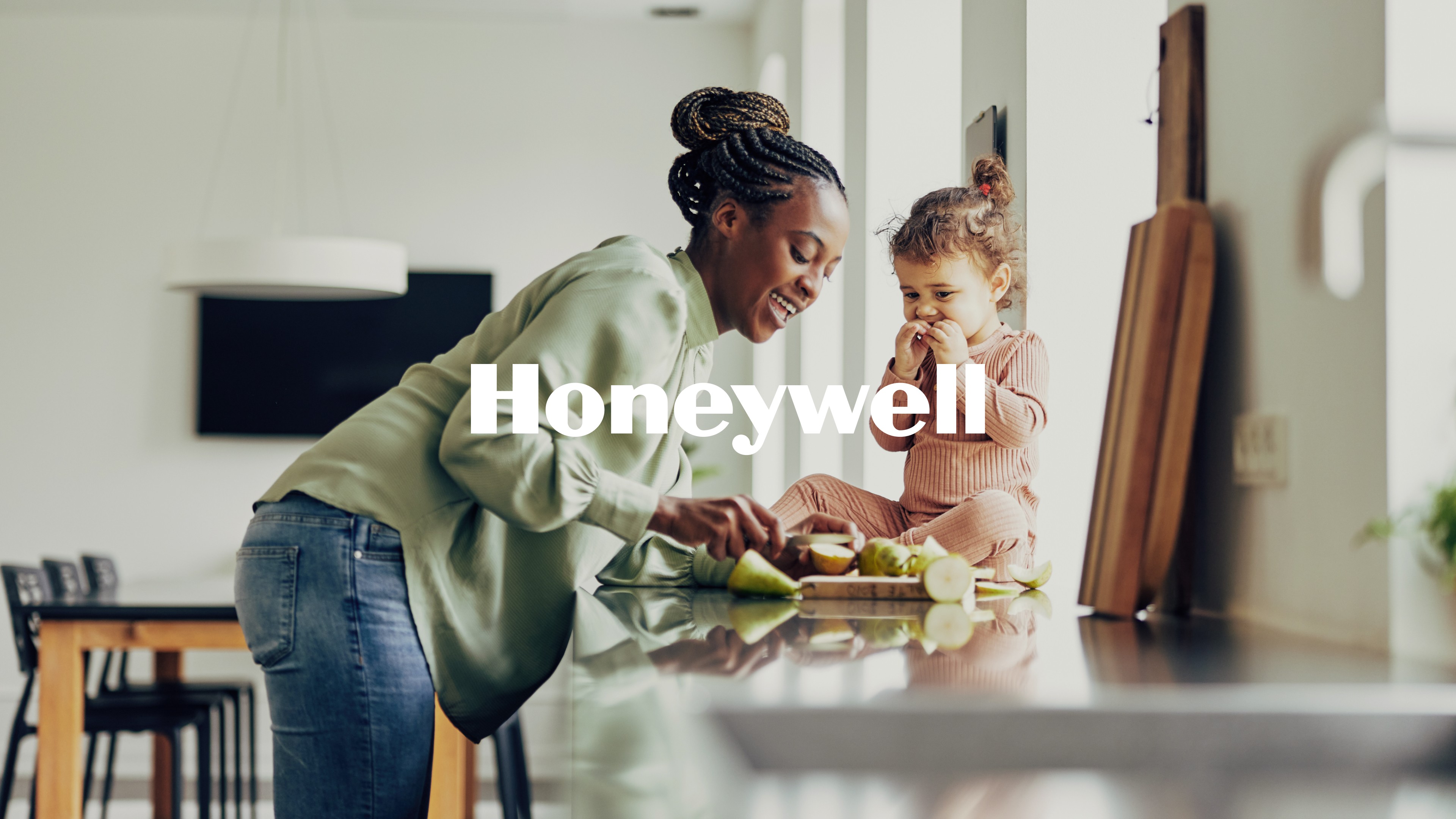 Mother preparing food while daughter sits on kitchen counter, Honeywell logo overlay