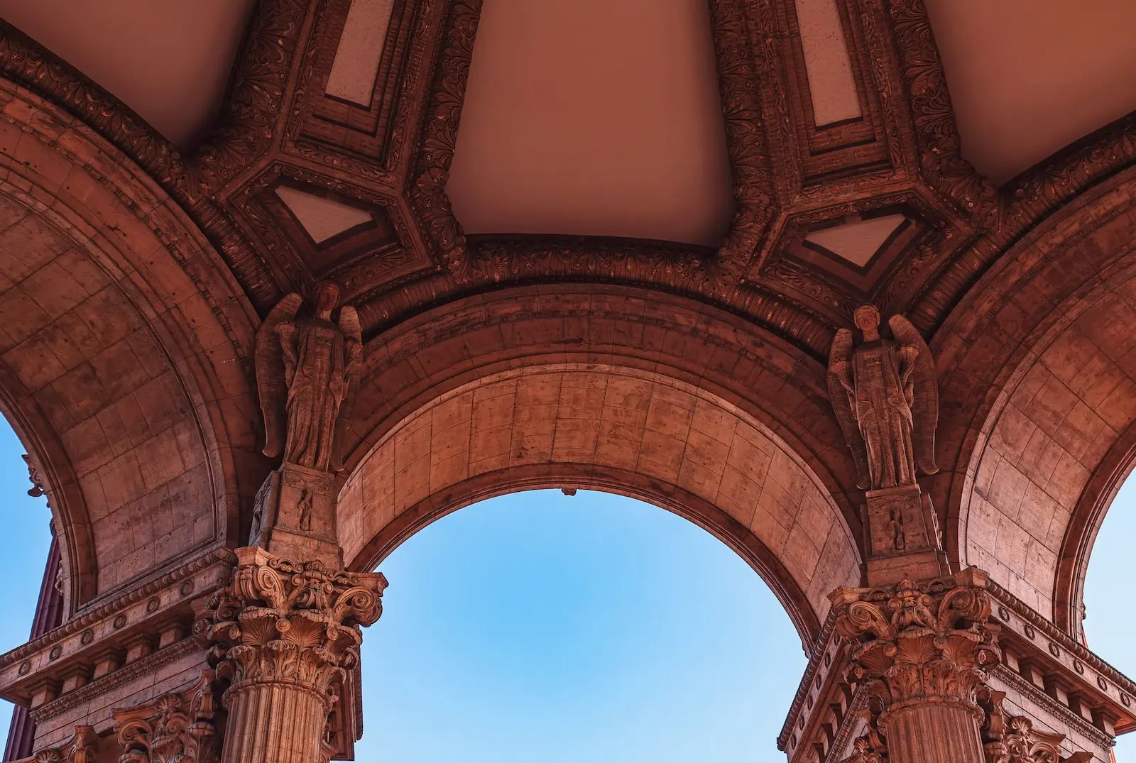 Ornate stone archway with carved columns and statues against a blue sky.