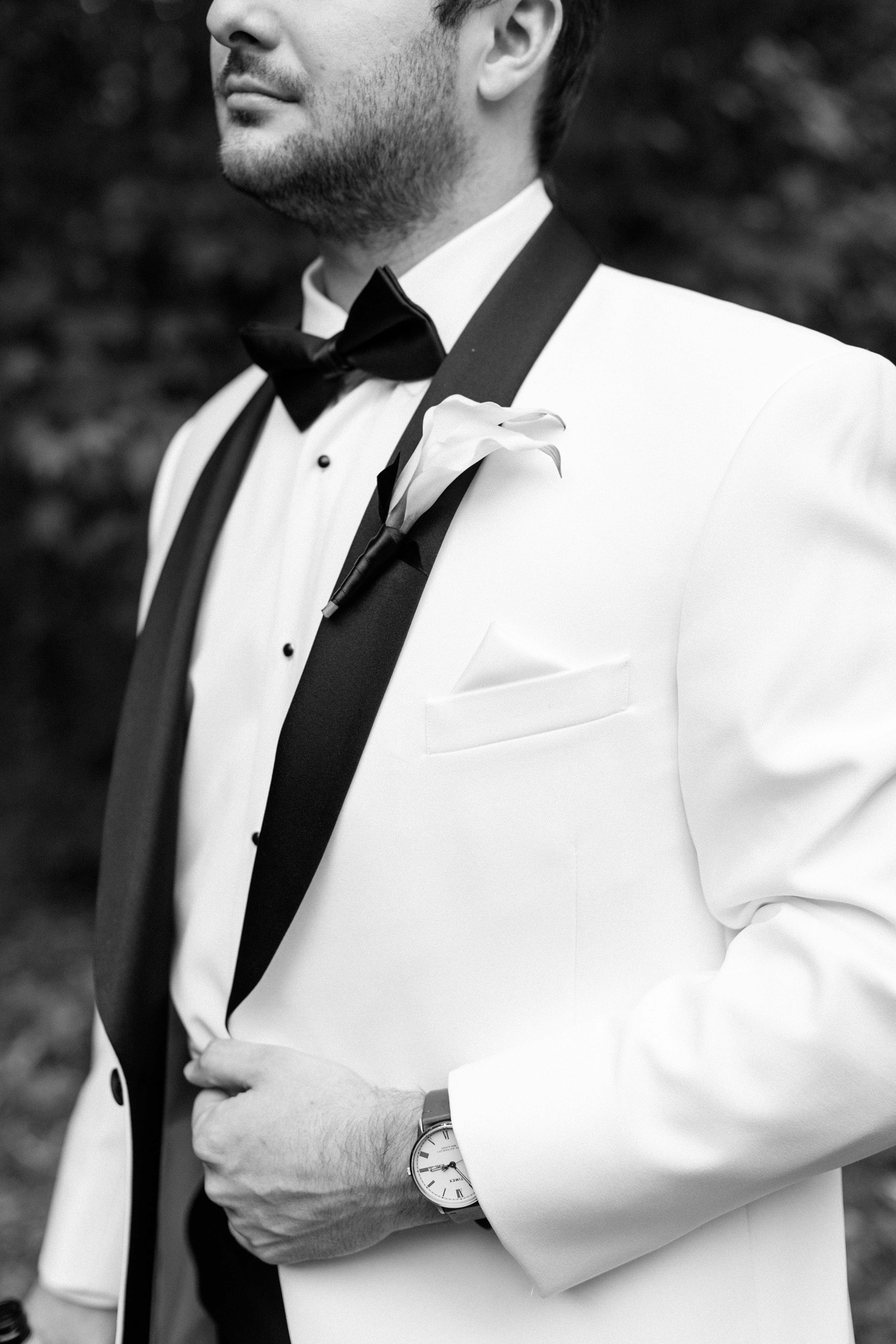 Black-and-white close-up of a tuxedo, calla lily boutonniere and wristwatch.