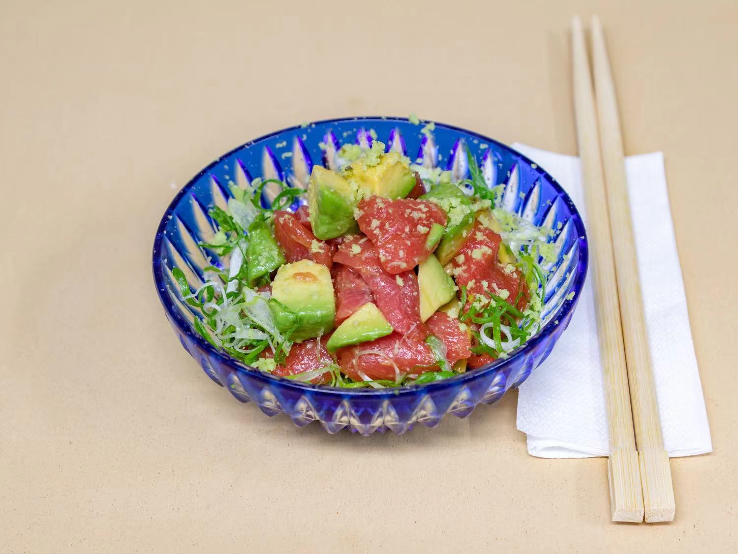 A colorful bowl of diced tuna sashimi and creamy avocado, tossed with microgreens and garnished with sesame seeds and a tangy dressing. Presented in an elegant blue bowl, this dish is both visually stunning and deliciously light.