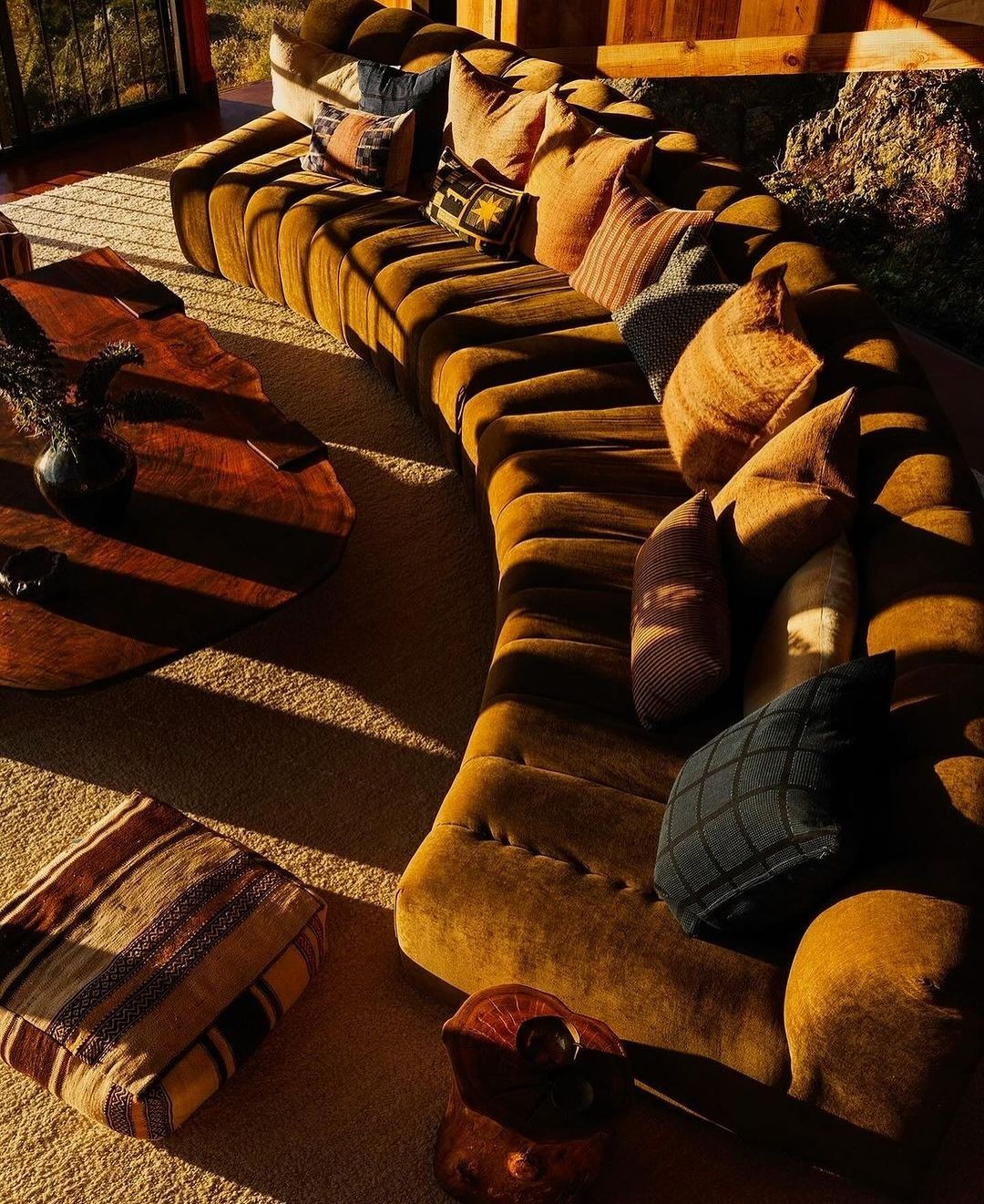 Warm sunlight across a rust-colored modular sofa with patterned cushions and wood tables.