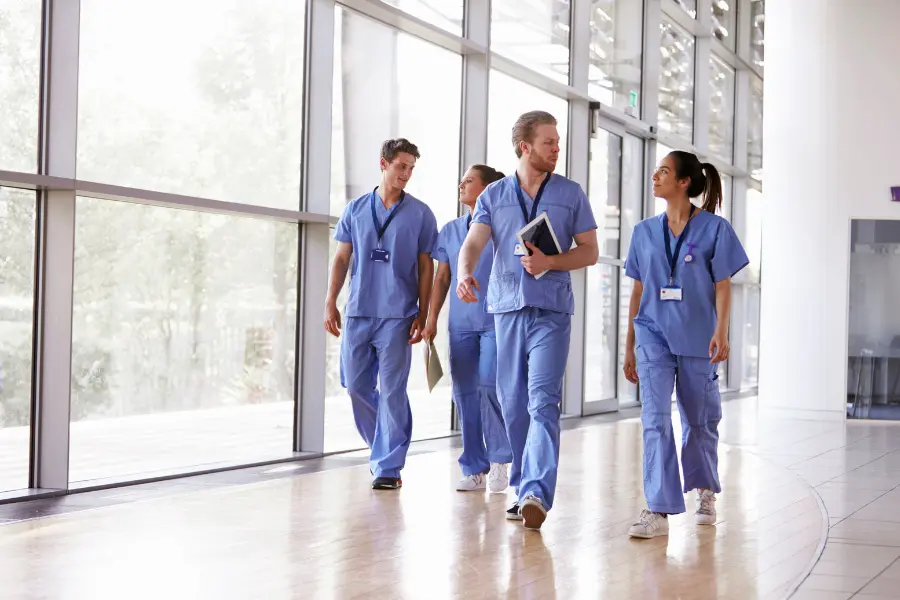 AI-powered medical coding workflow supported by a team of four healthcare professionals in blue scrubs walking through a bright hospital corridor with a tablet in hand.