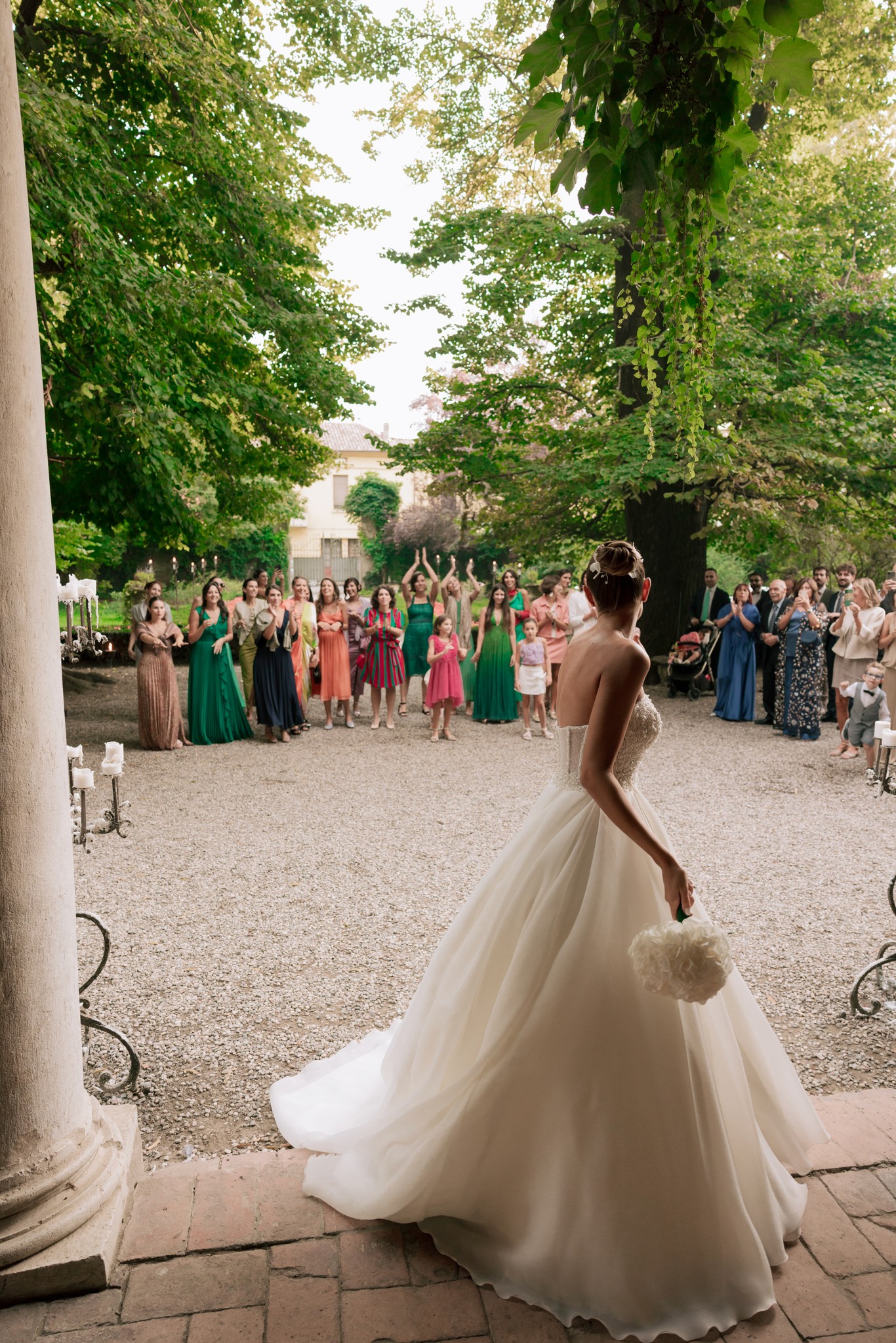 Sposa in abito bianco con strascico nel giardino di Villa Ferrari, circondata dagli invitati al ricevimento matrimoniale