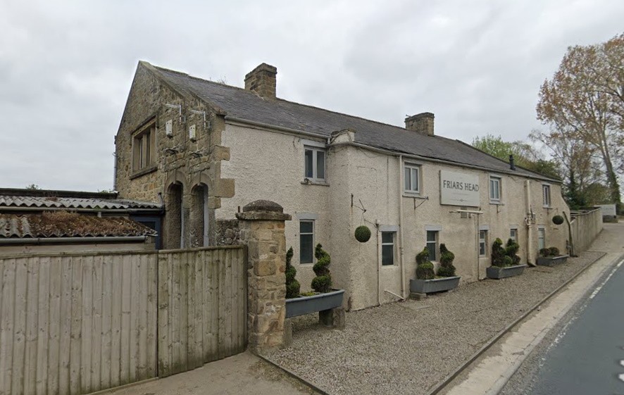 Traditional whitewashed stone cottage with manicured potted plants along quiet country lane in charming rural setting