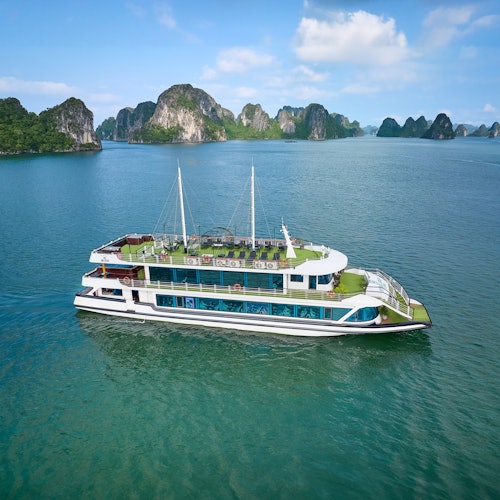 En to-etagers båd, der sejler på roligt vand med klippeøer i baggrunden under en delvist skyet himmel.