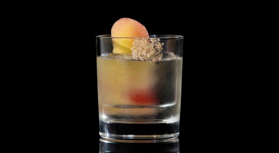 A closeup of a Peach Vodka Old Fashioned drink against a dark background.