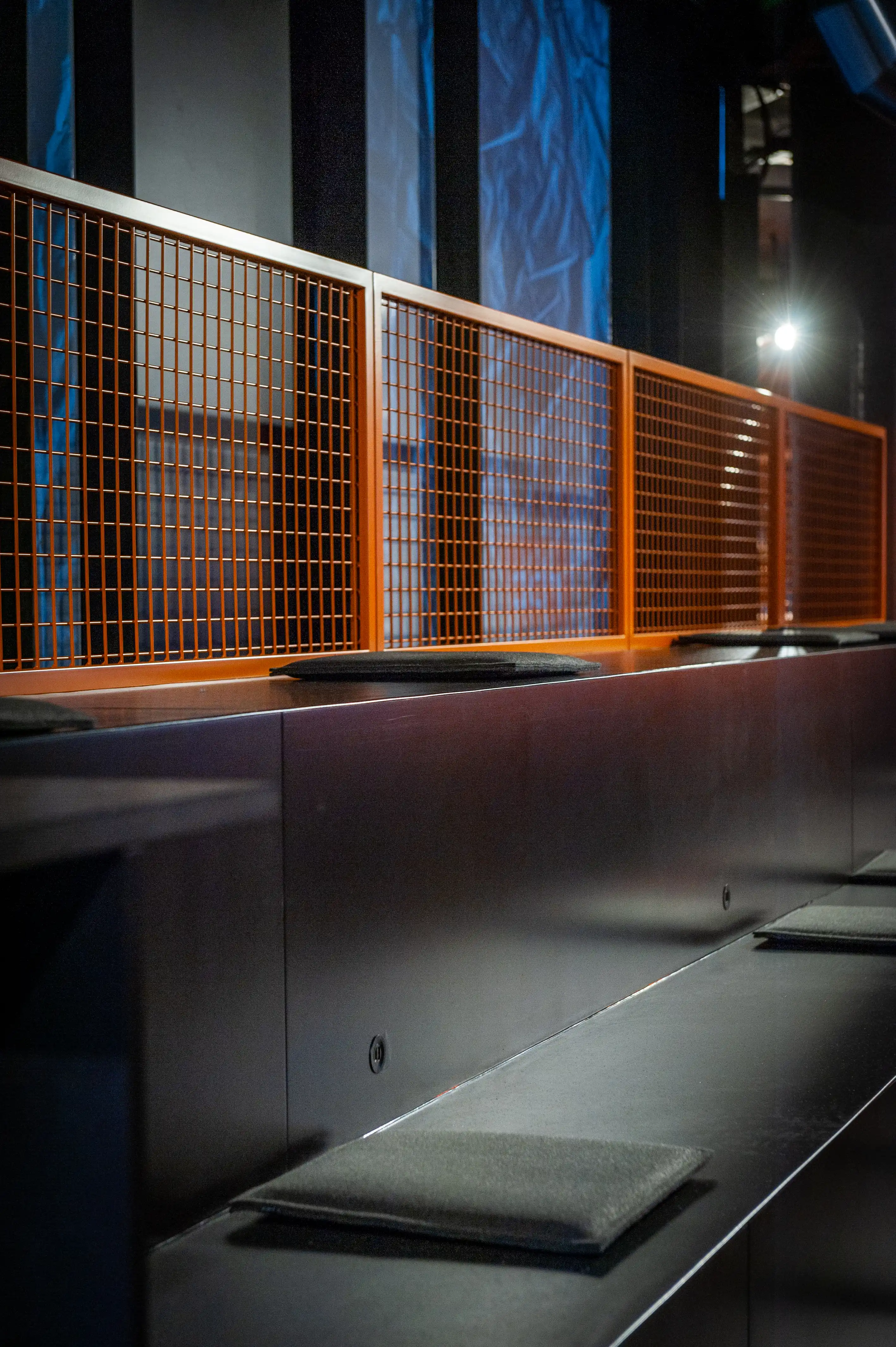 Detail of orange wire-mesh panels along a dark counter with felt seat pads in the Radio Eins studio.
