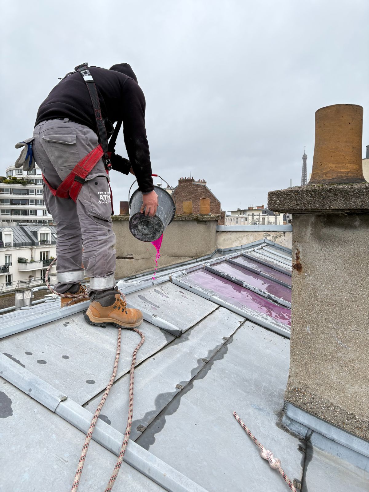 Intervention encordée sur une couverture zinc, Paris 15e Technicien équipé d'un harnais et encordé versant un traceur rose sur une toiture en zinc à tasseaux