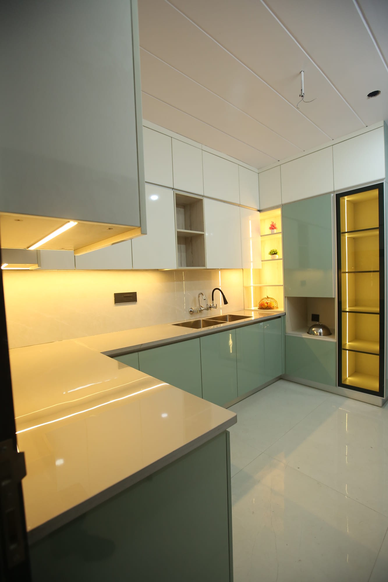 Sage-green gloss kitchen with cream wall cabinets and warm under-cabinet lighting