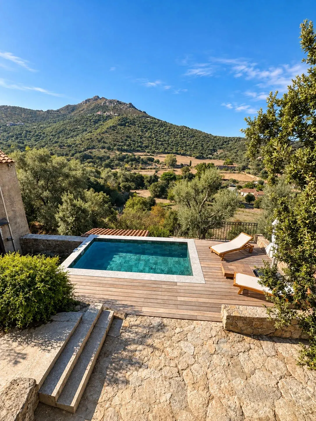 Piscine bordée d'une terrasse en bois, d'un dallage et de marches en pierre, face aux collines de Balagne