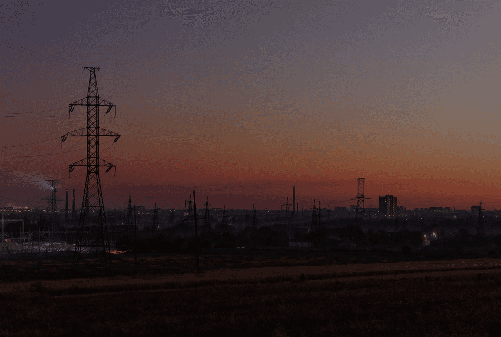 Strommast im Fokus einer Stadt bei Sonnenuntergang