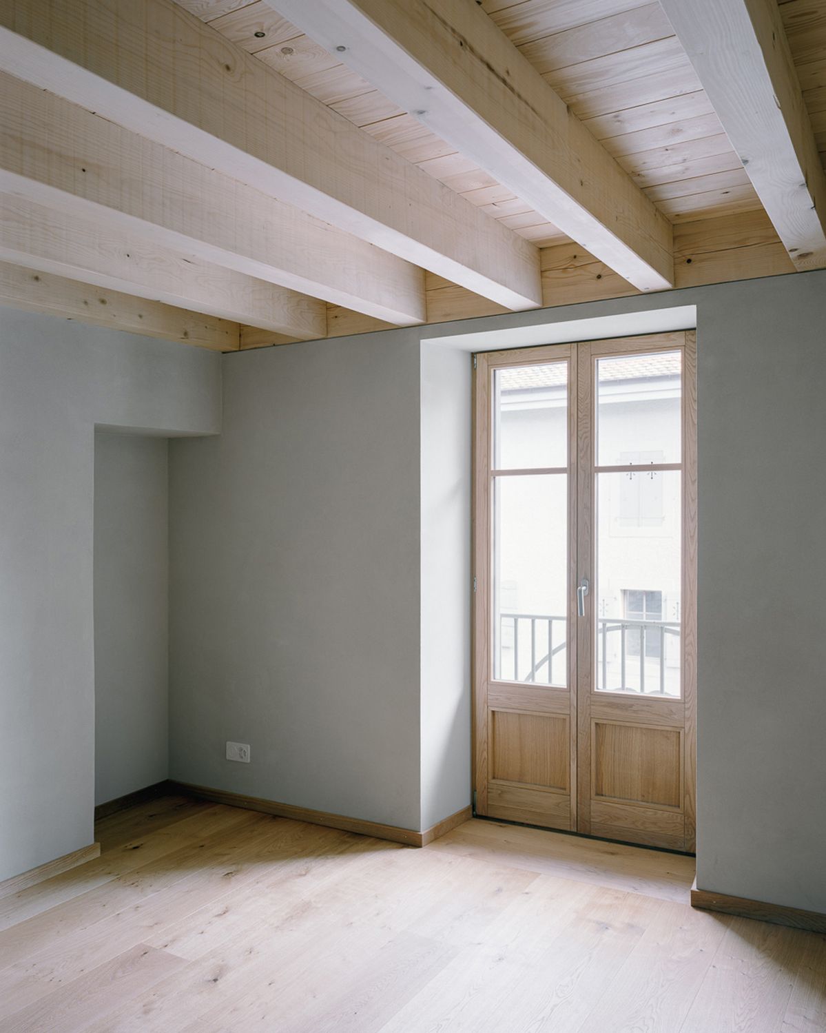 Mur blanc avec une porte en bois et un arbre en premier plan