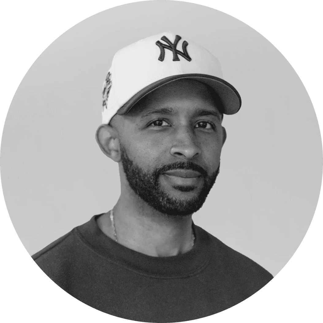 Person wearing a blue puffer jacket and red backpack standing in front of a light blue building on a city street.