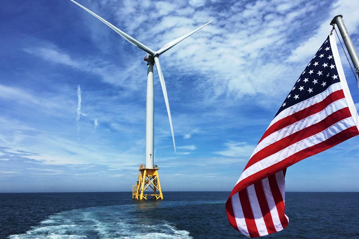 Offshore wind turbine at sea with a United States flag in the foreground.