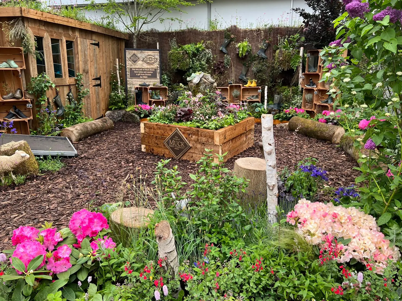 A vibrant garden with colorful flowers, wooden structures, and a peaceful pathway amidst greenery.
