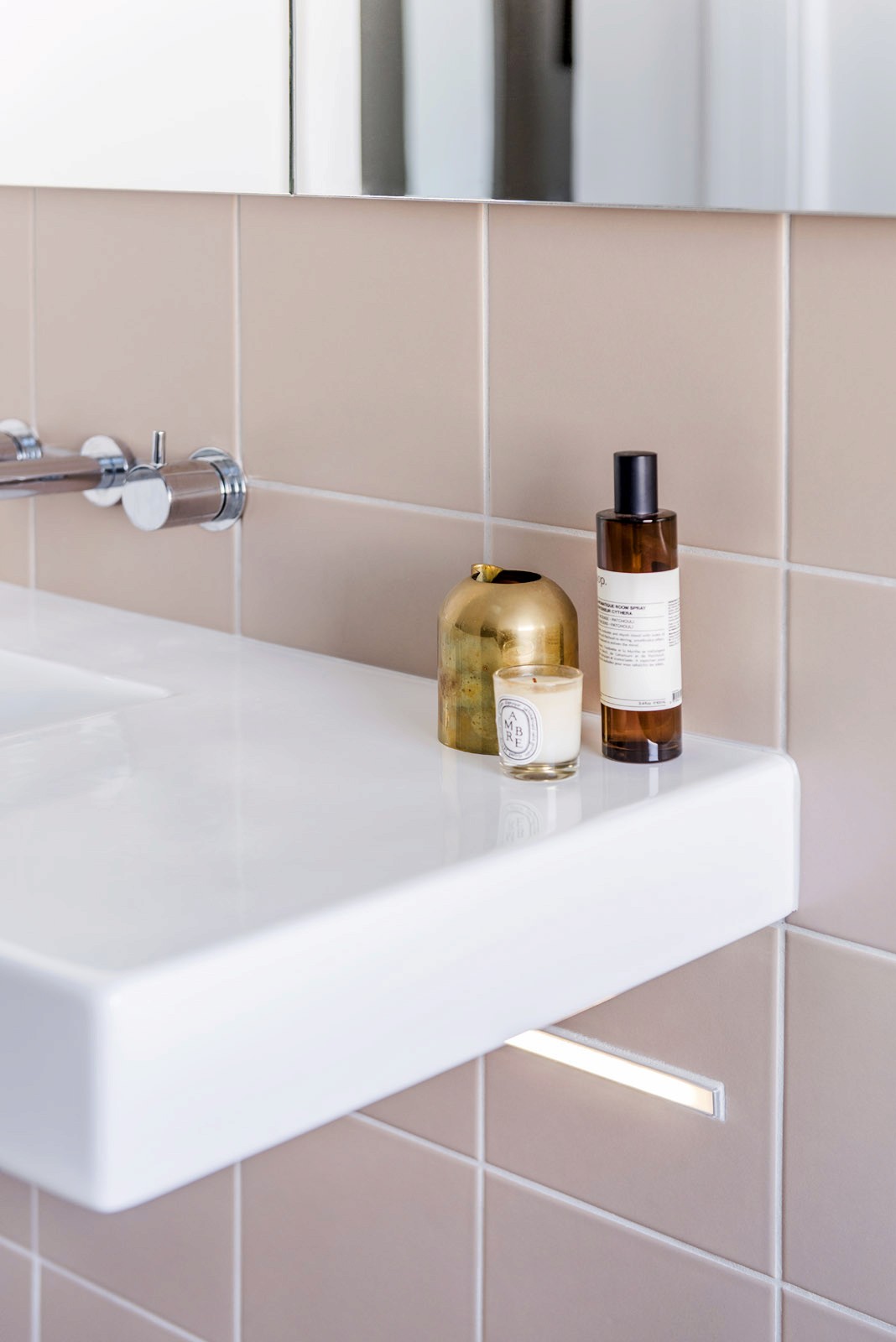 Close-up of bathroom sink with pink tiled wall, chrome fixtures, and toiletries on countertop