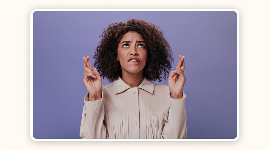 Woman with curly hair crossing fingers and looking up hopefully&nbsp;
