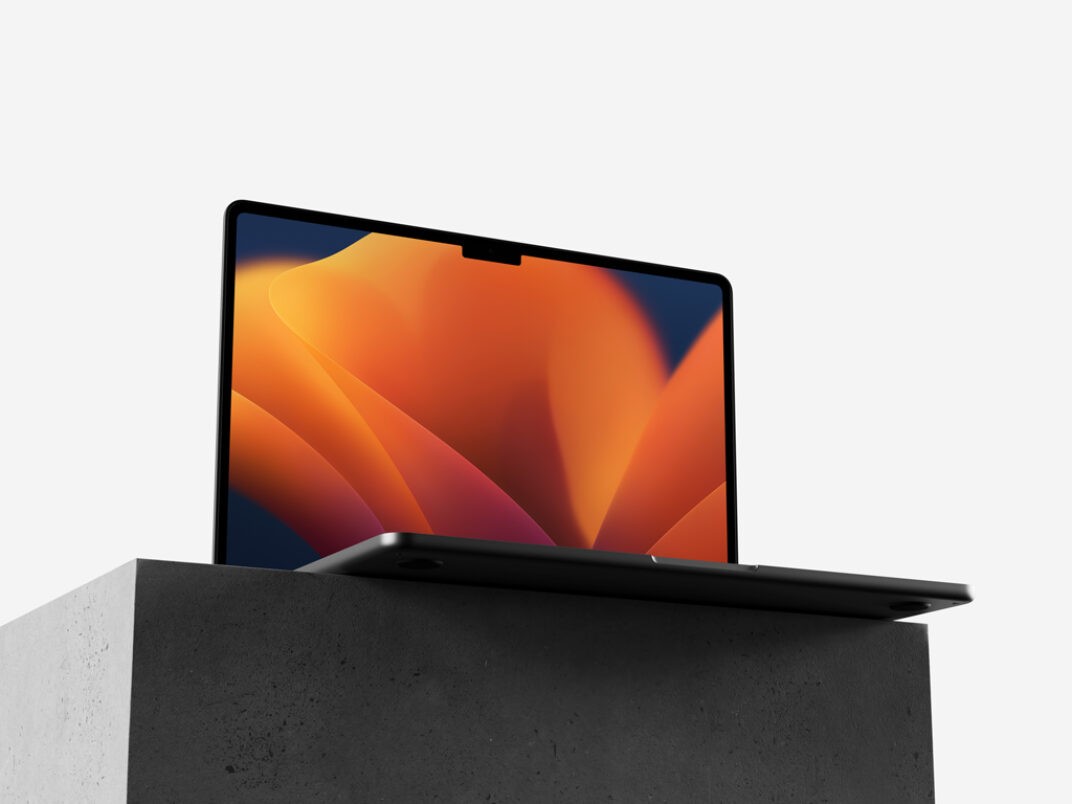 MacBook mockup displayed on a dark concrete pedestal with a sleek design. The screen showcases vibrant abstract orange and yellow gradient graphics, set against a minimal white background.