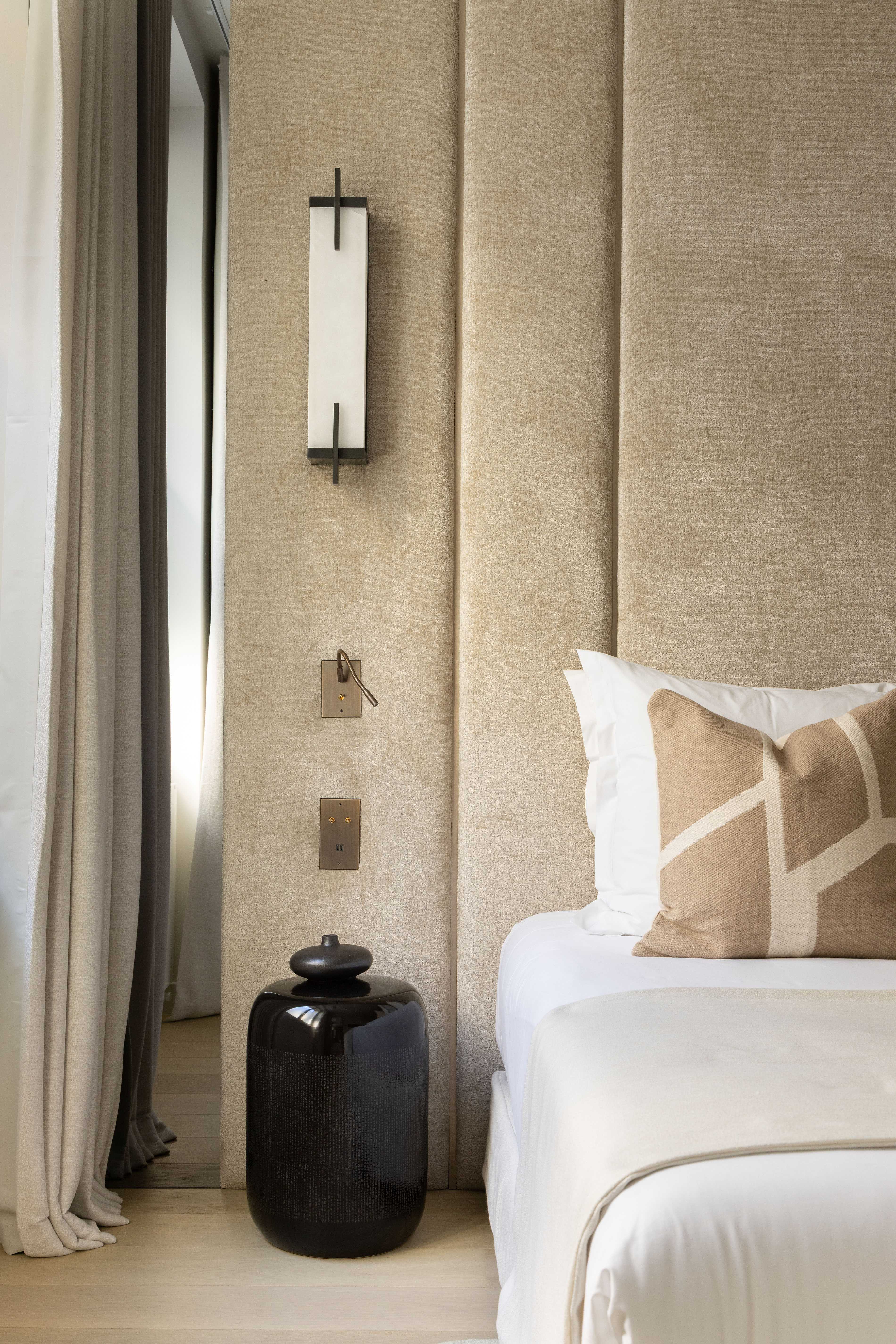 Détail chambre avec table de chevet noire en céramique, applique murale et coussin