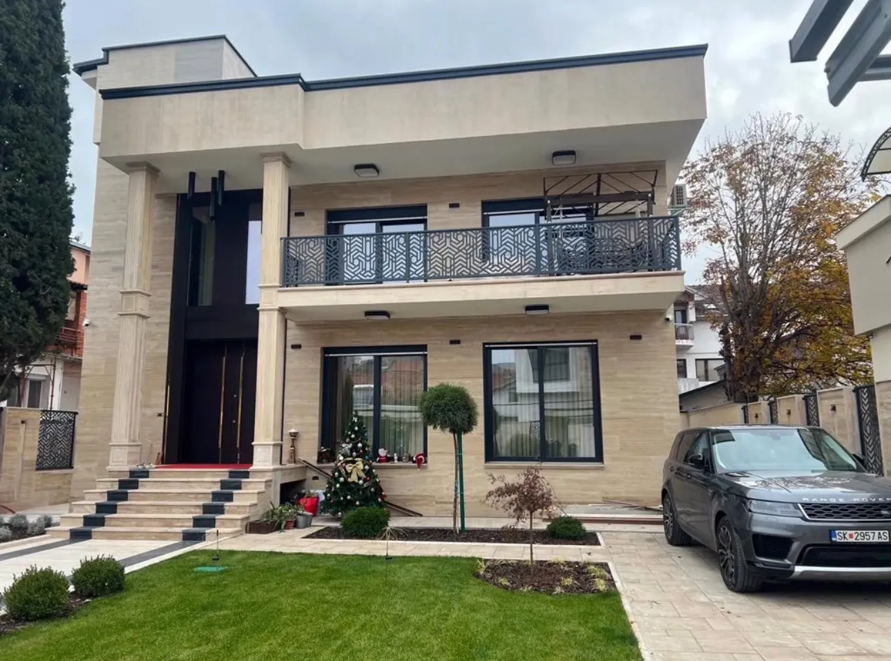 Front garden and entrance of a private residence in Skopje, showcasing stone finishes, balcony detailing, and seasonal decor. Architectural planning and supervision by Terraplan Partners.
