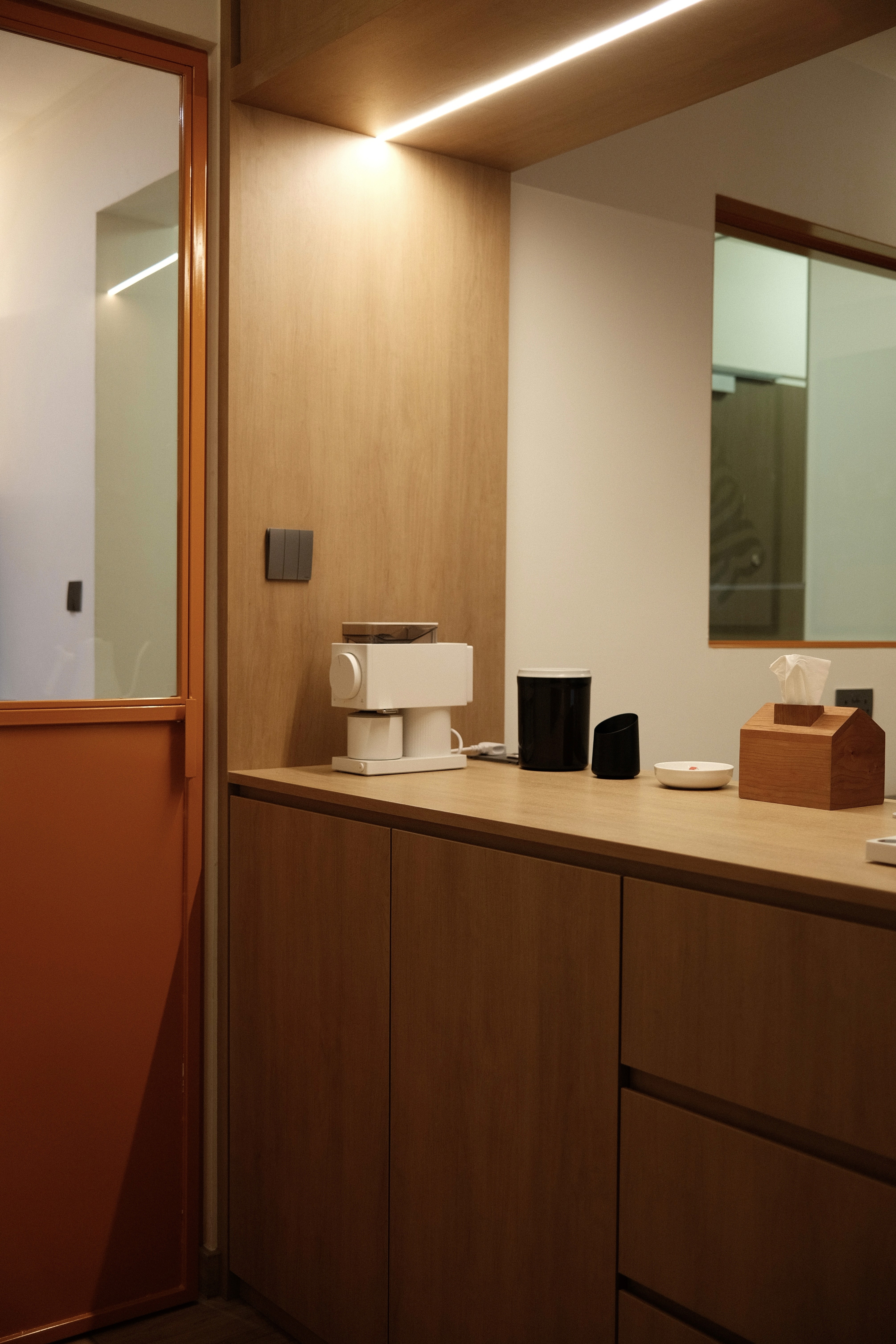 A compact utility counter finished in warm timber tones, combining practical storage with subtle lighting to elevate everyday routines.