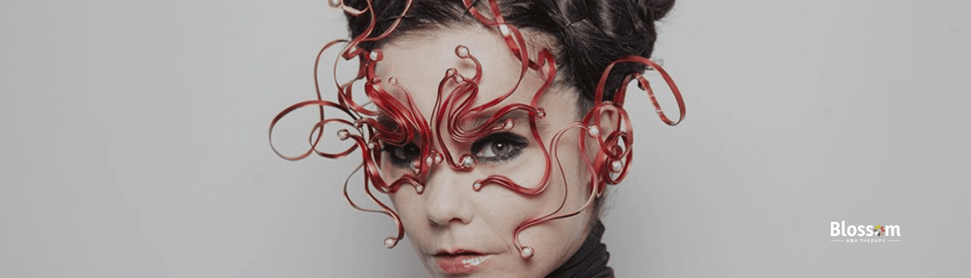 Bjork, suspected with autism, wearing an intricate red artistic mask with a futuristic design.