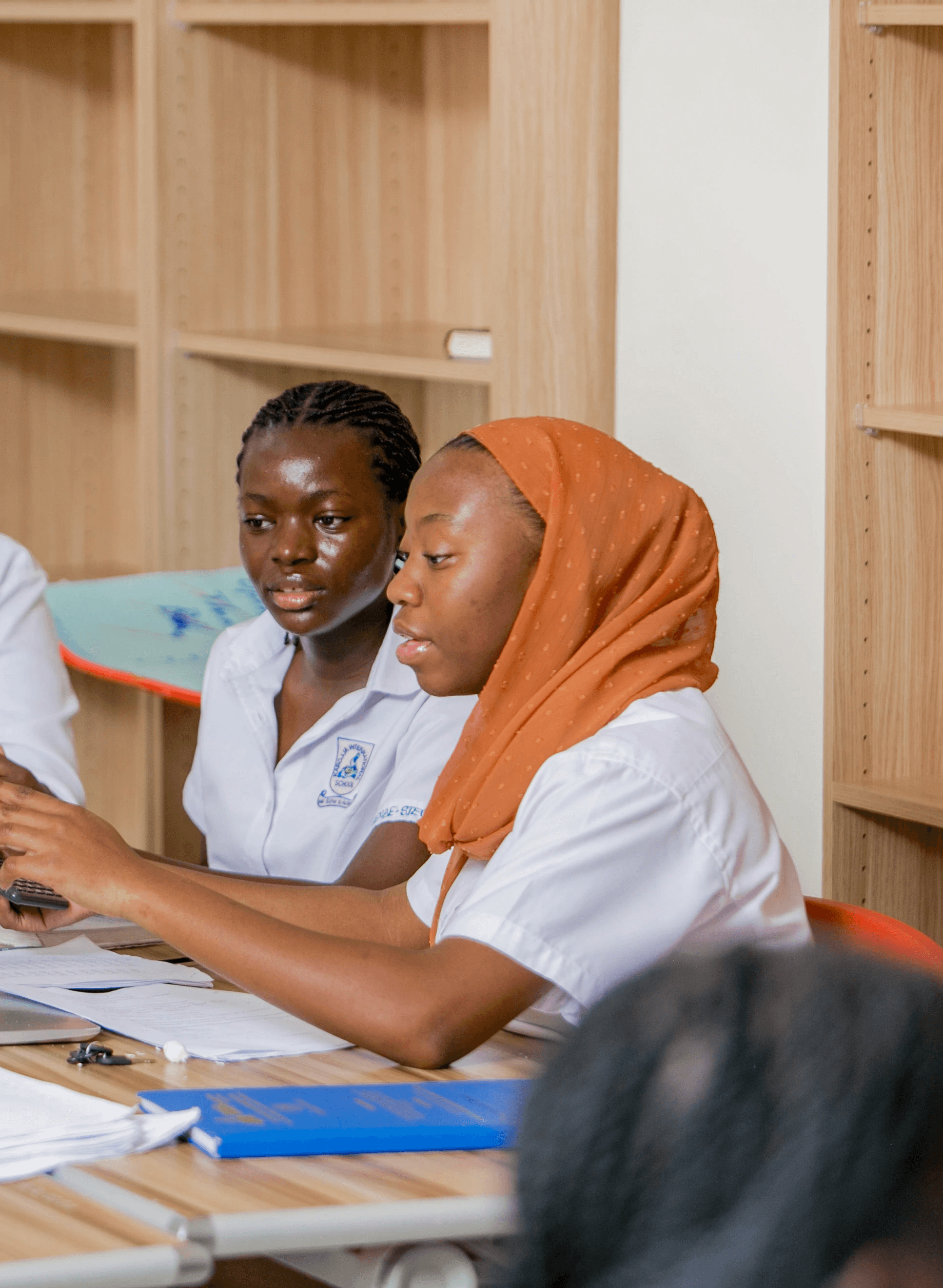 A student wearing a red uniform sits while holding a book in his hands