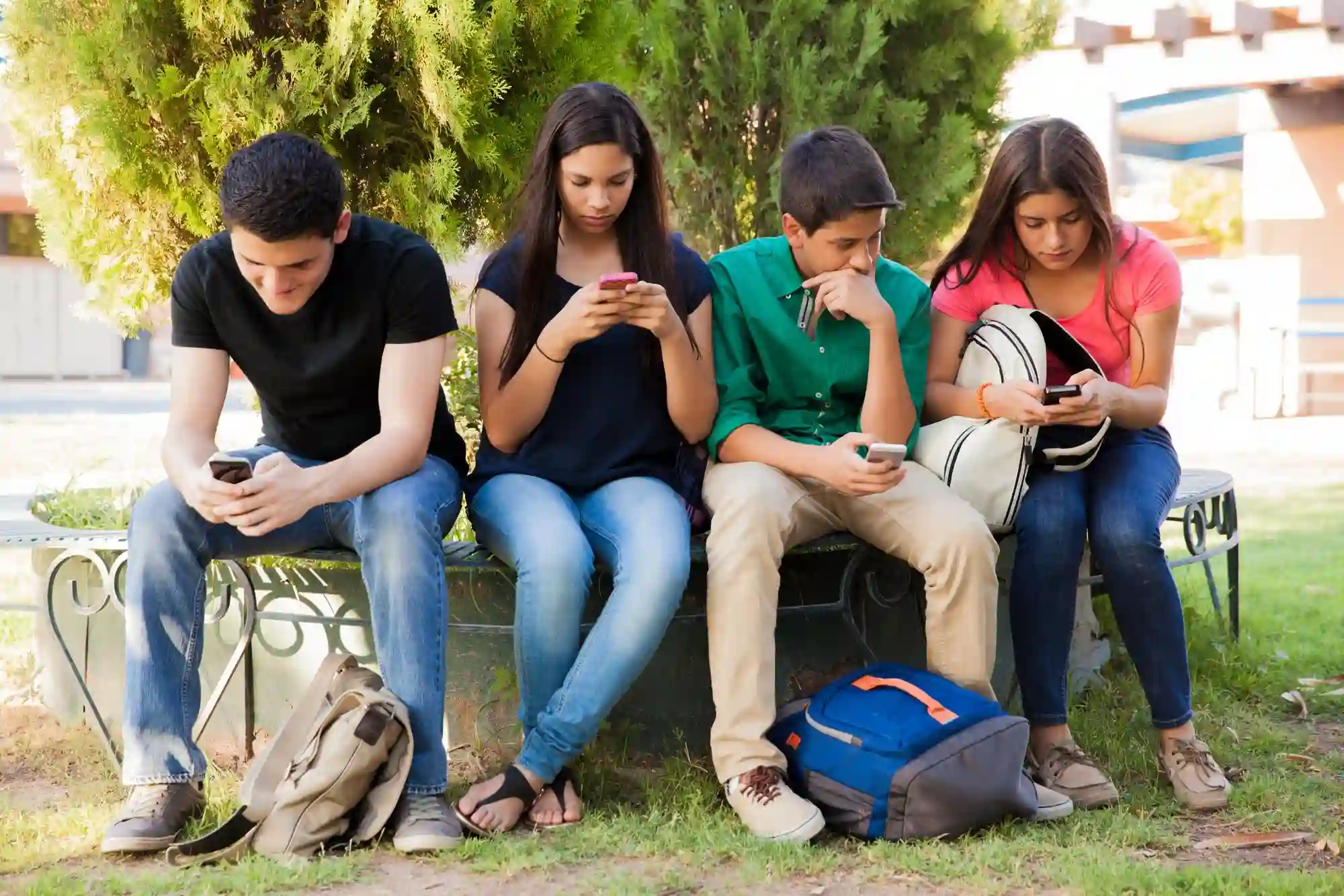 Four young people sitting on a bench, looking at their phones.