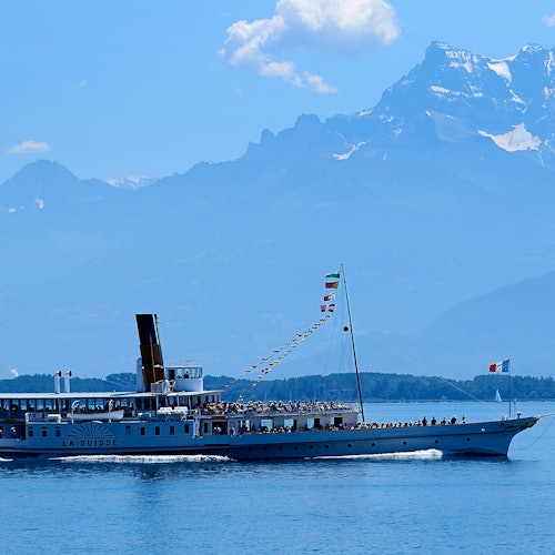 一艘名为“拉苏”号的船在平静的湖面上航行，背景是群山，天空湛蓝无云。
