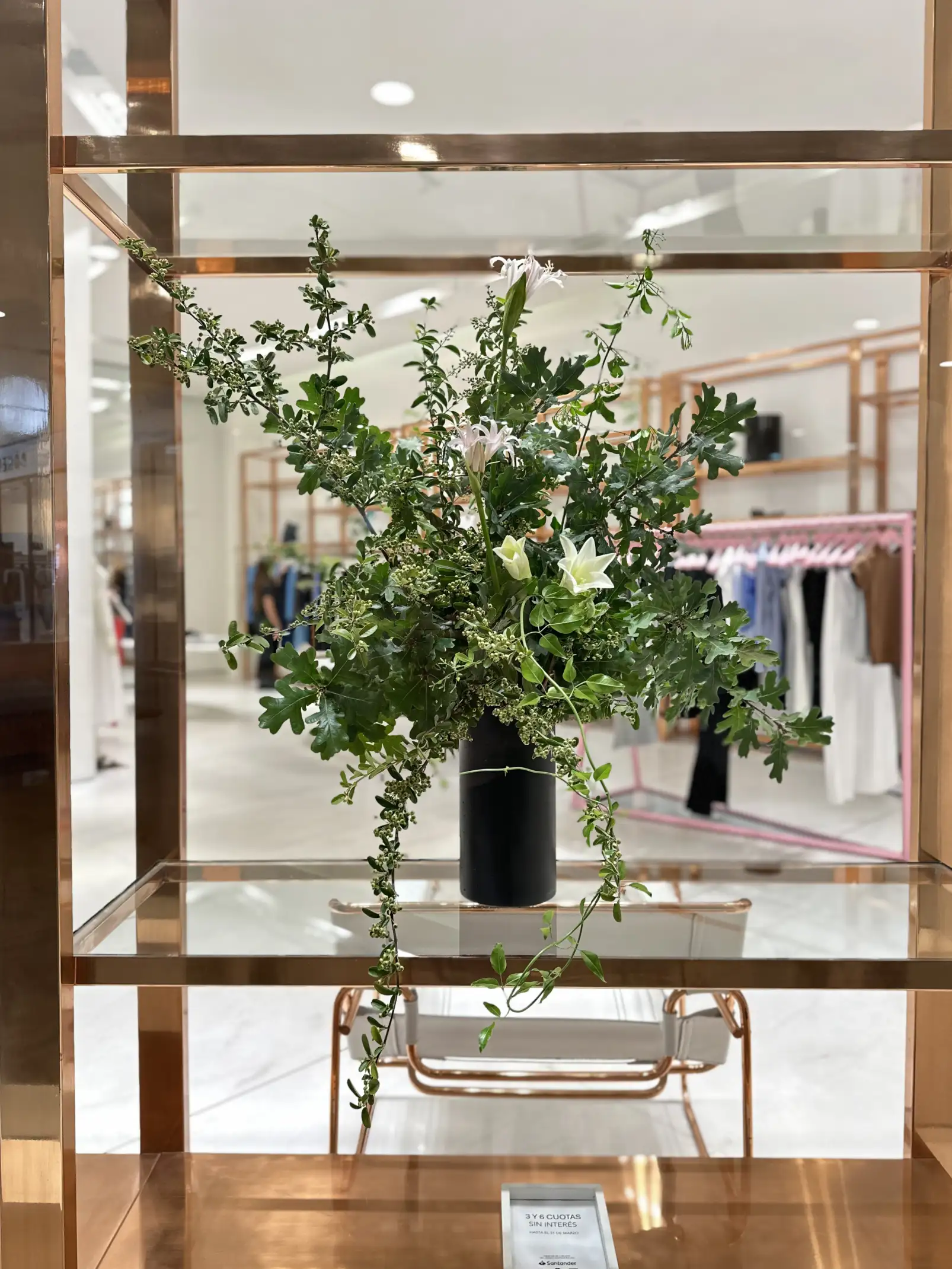 Arreglo floral con follaje verde y lirios blancos exhibido en vitrina moderna para ambientación natural de tienda