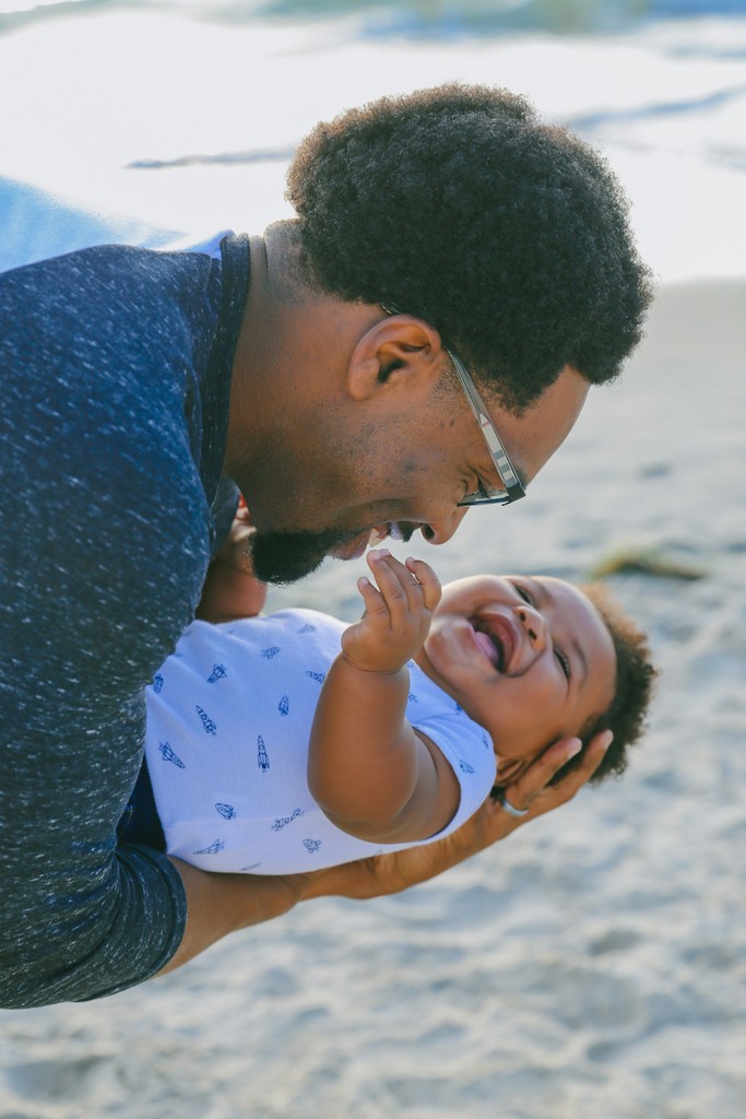 A joyful father plays with his laughing baby on a sunny beach, capturing a heartwarming moment of bonding and happiness by the ocean.