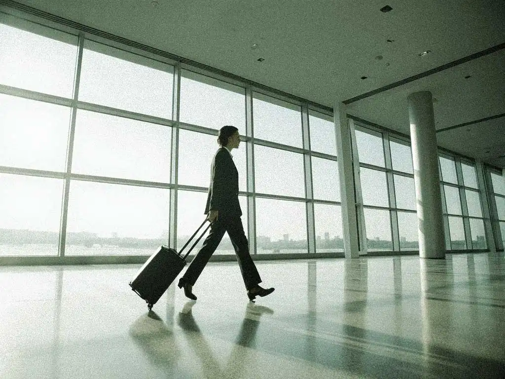 Business professional walking through a modern airport terminal carrying luggage.
