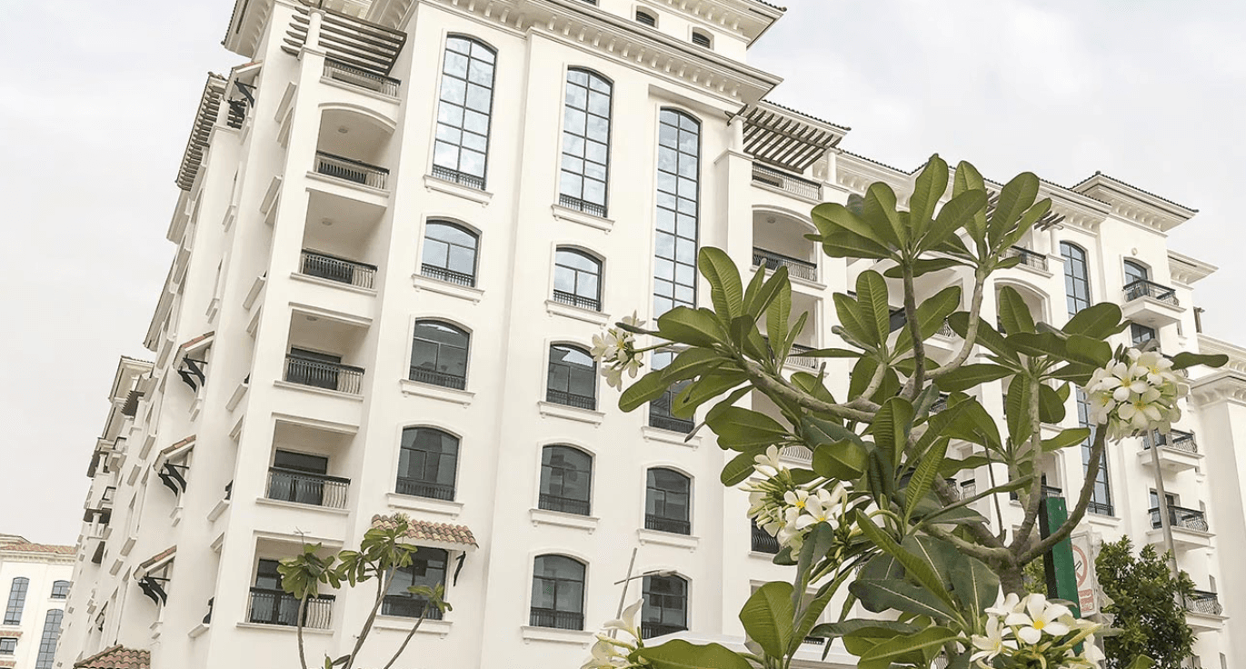 A large white building surrounded by lush green plants in the foreground.