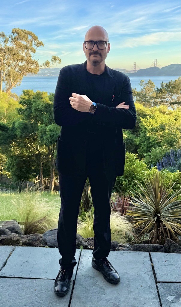 a man with his arms crossed standing in front of a desk