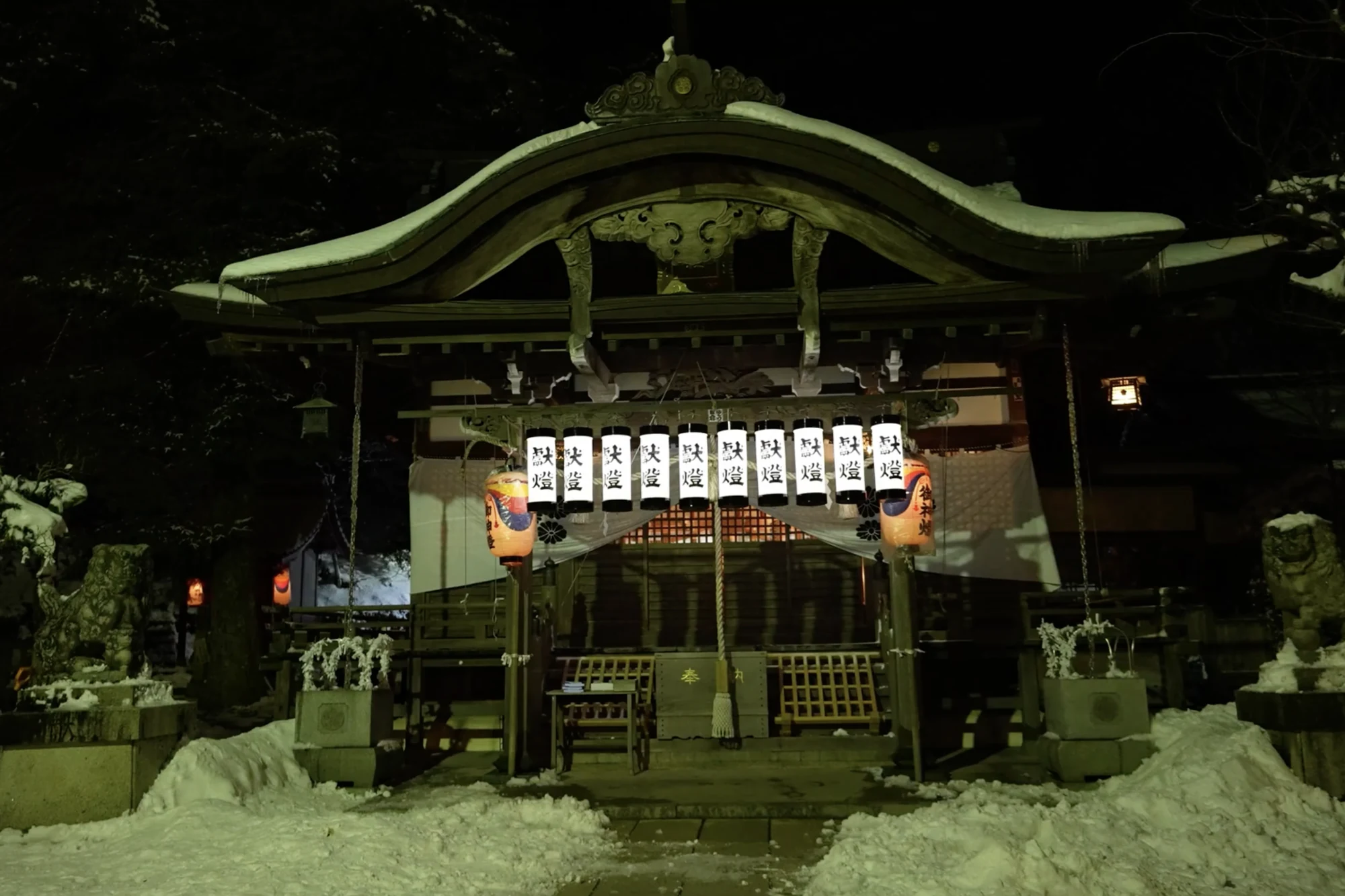 Shisho Shrine in Kinosaki lit by paper lanterns at night with snow across its forecourt.