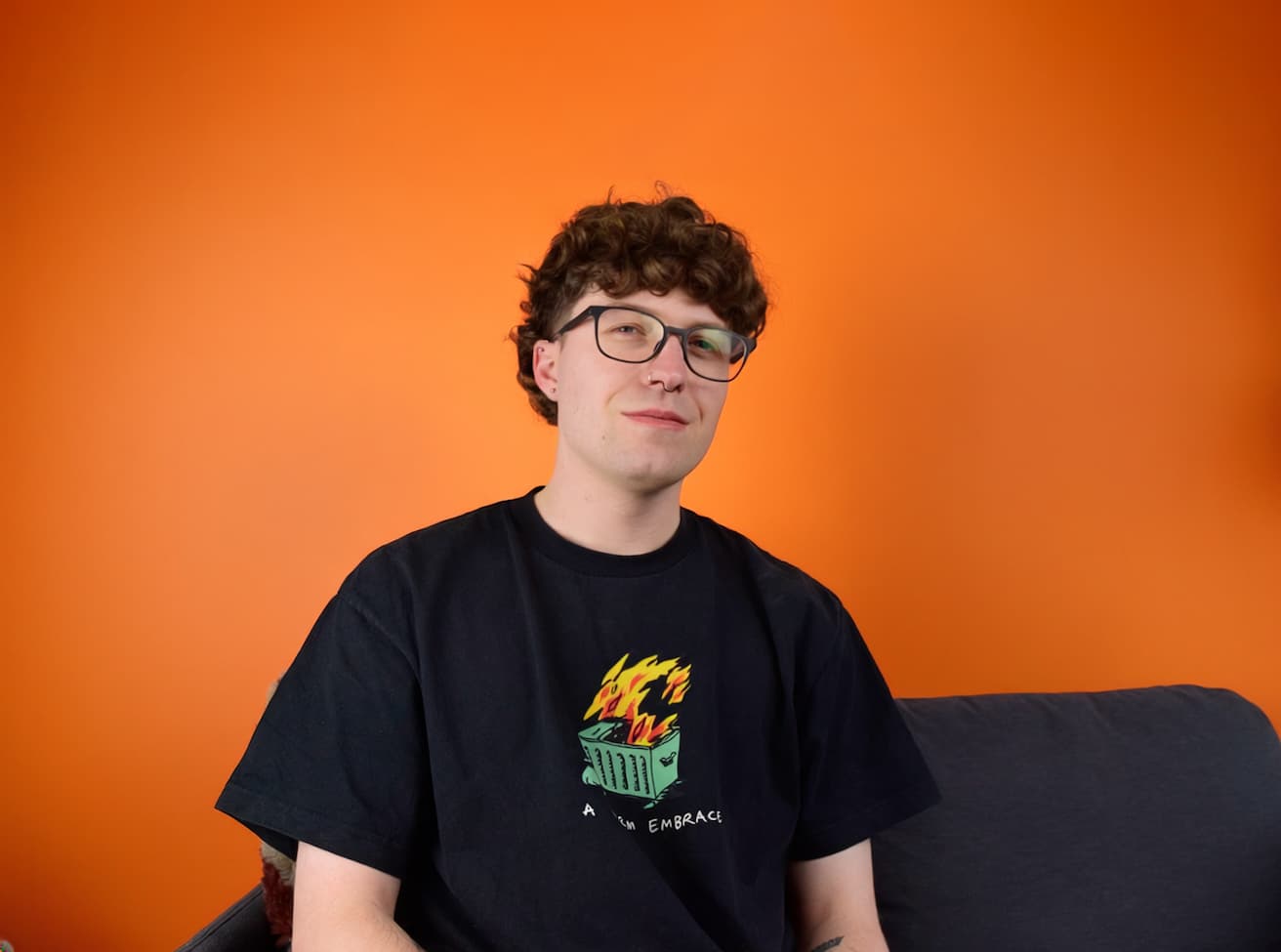 Graphic design freelancer in glasses and a black t-shirt, seated on a sofa in an office.