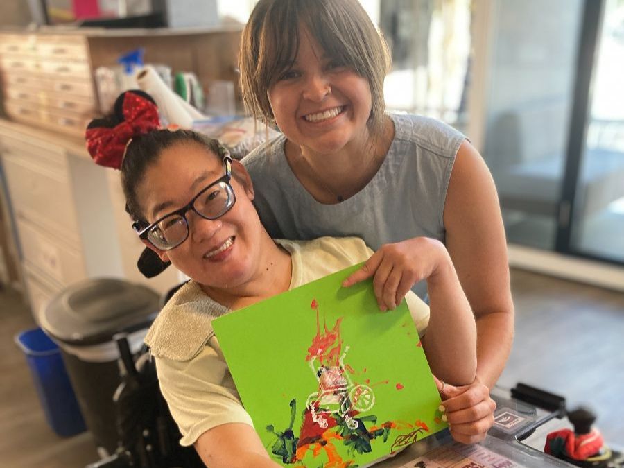 Access Gallery artist Mikelle holds her artwork alongside her caregiver, Maryann, in the Access Gallery studio.