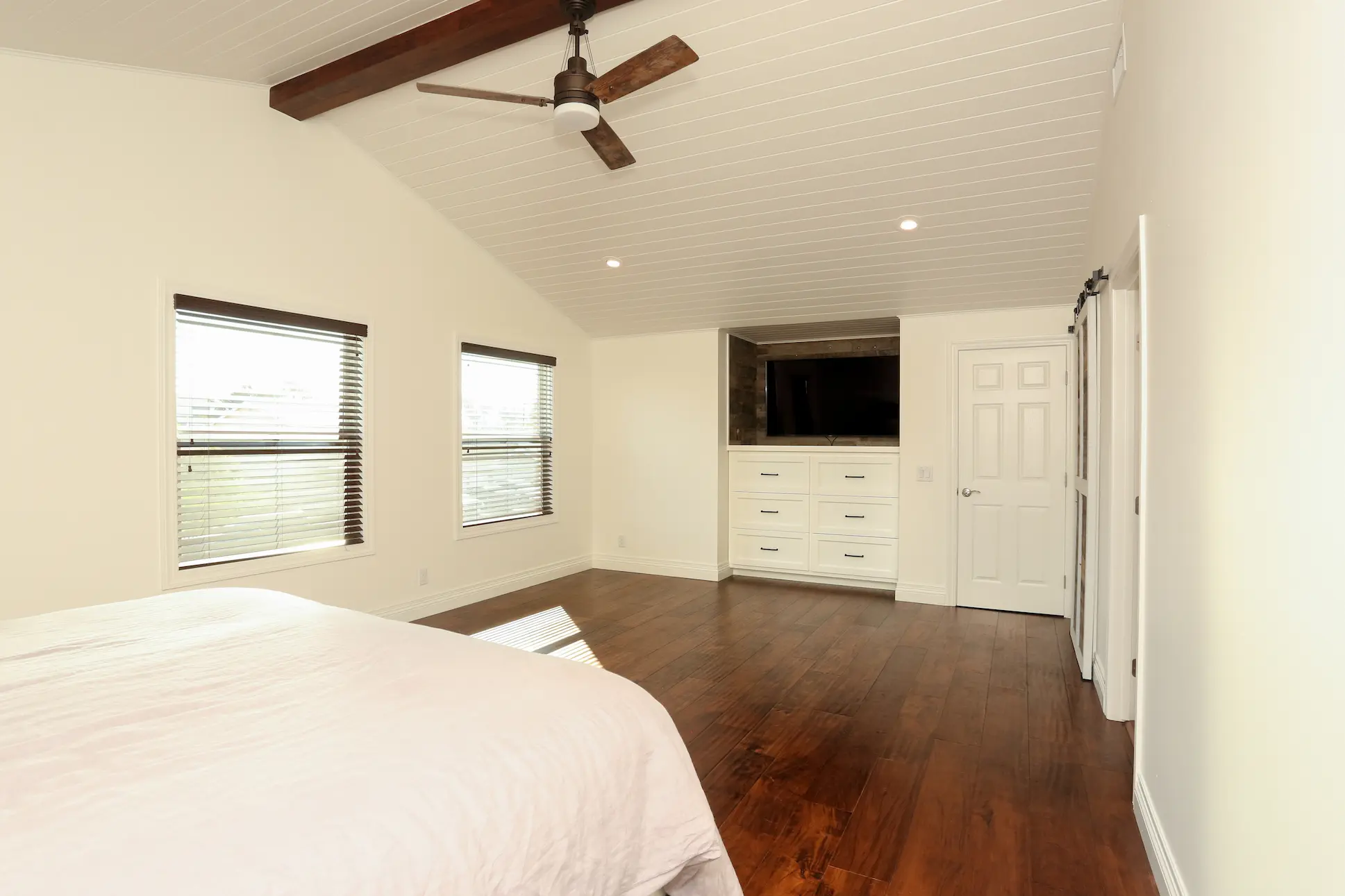 Angle 2 of Primary bedroom with dark wood flooring, barn door closet, and white paint. Photo by Chris Darnall.
