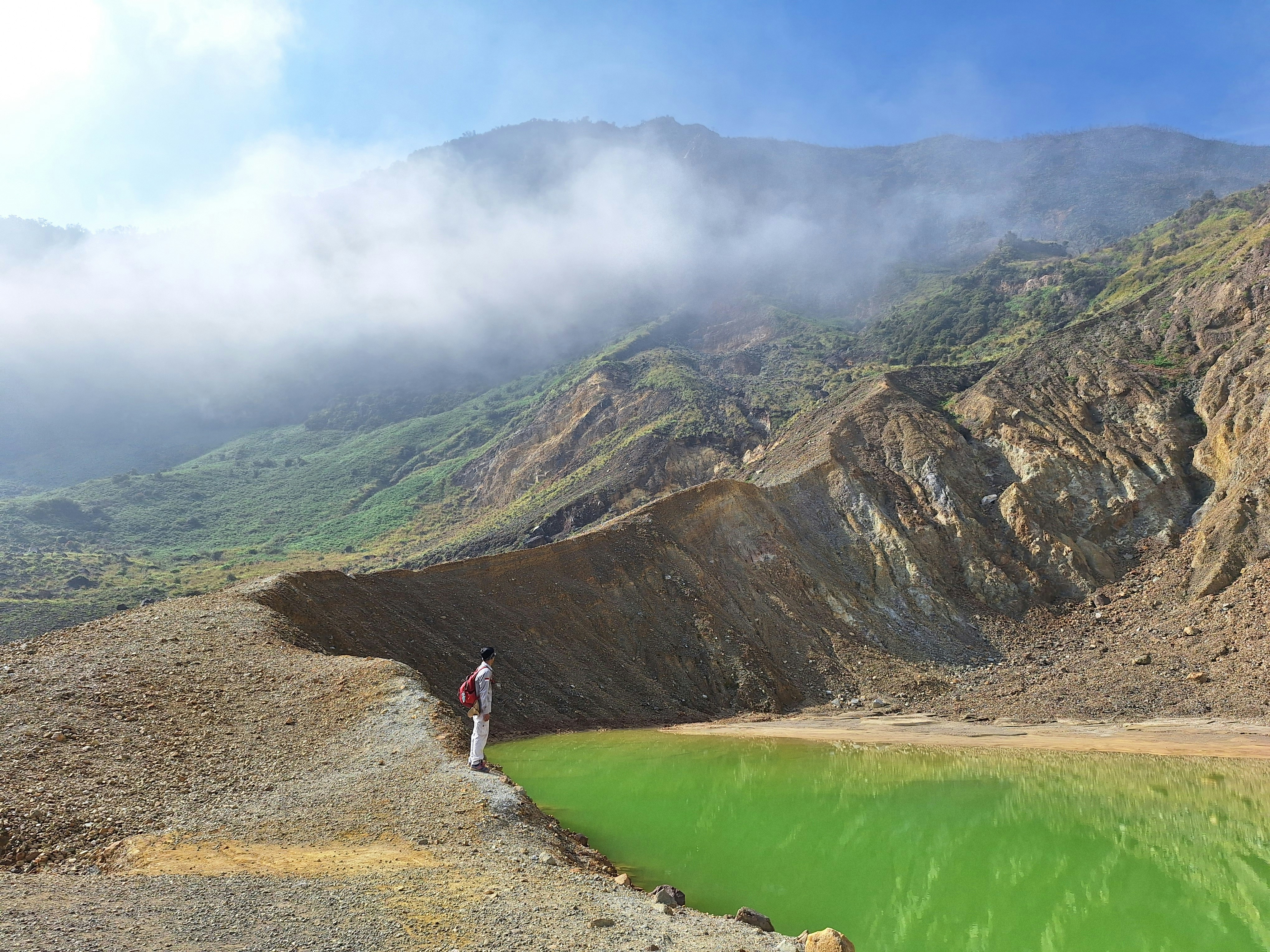 a man standing on the edge of a cliff next to a green lake