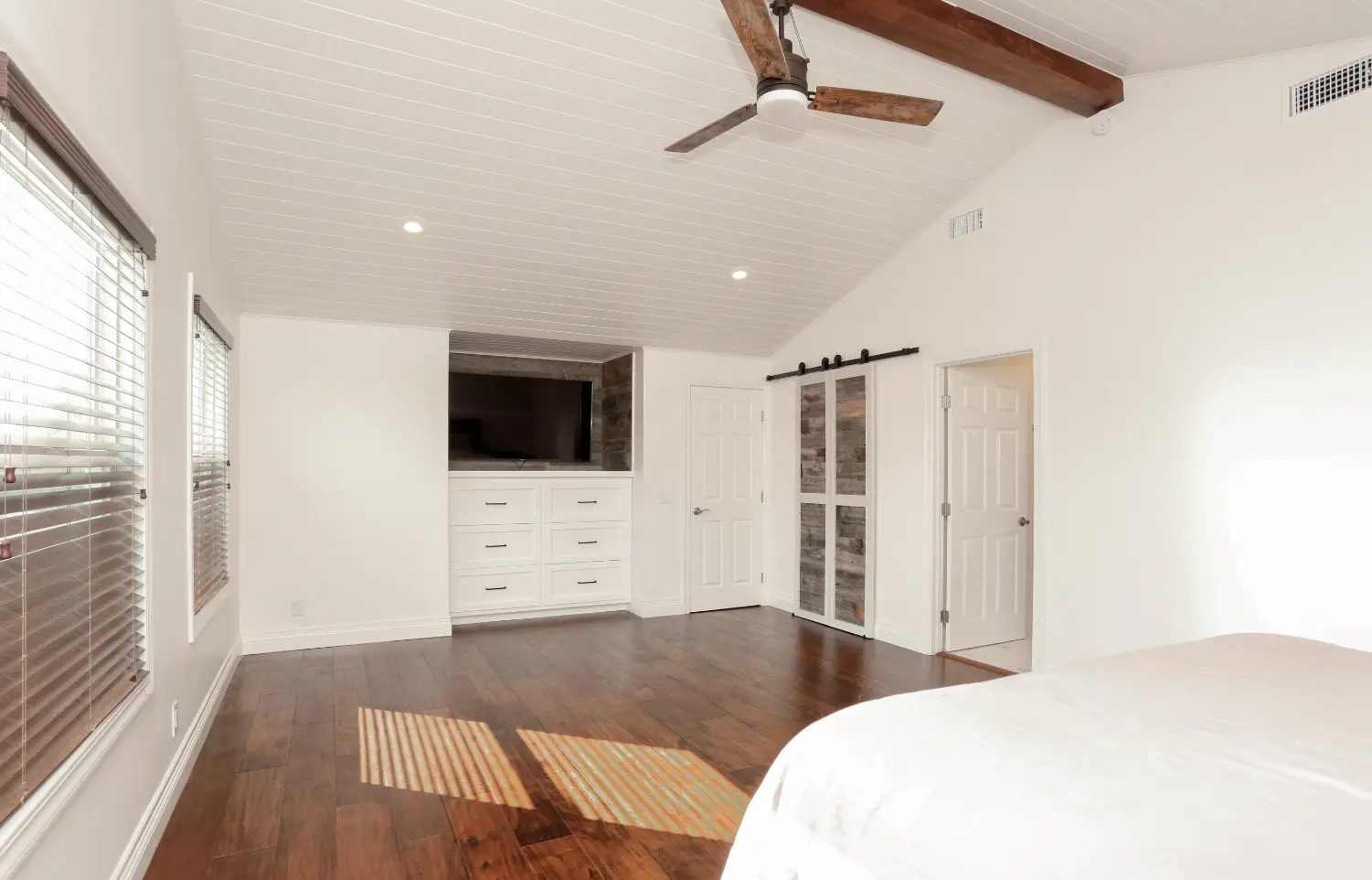 Primary bedroom with dark wood flooring, barn door closet, and white paint.Primary bathroom with muted tones, double vanity, makeup vanity, and spacious walk-in shower and marble tile. Photo by Chris Darnall.
