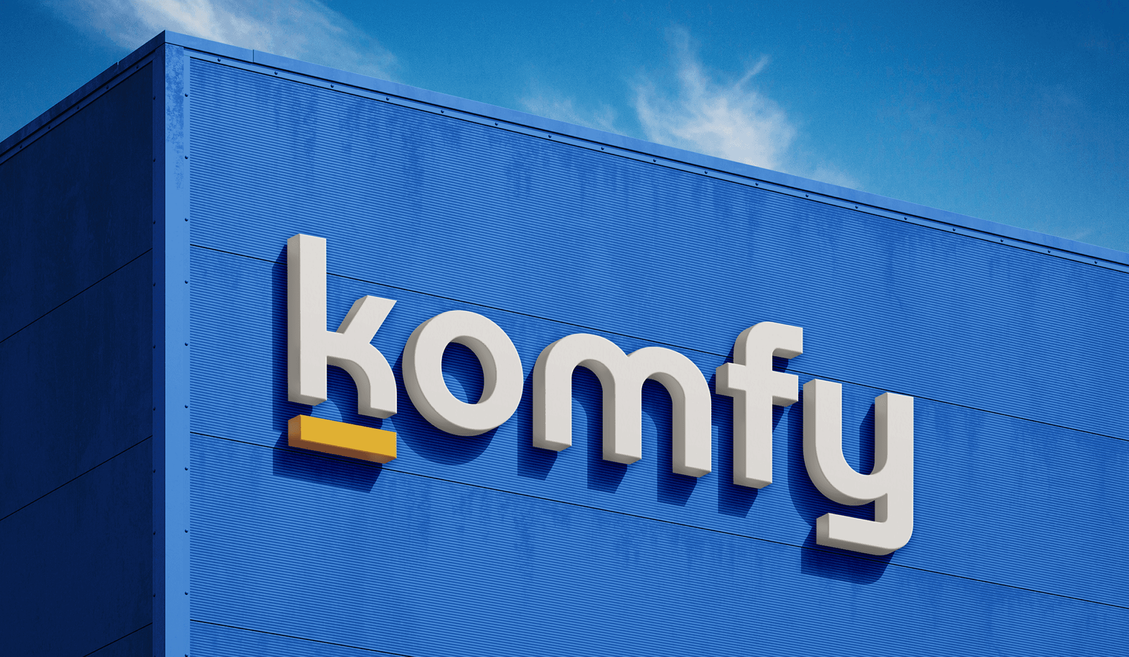 A large, modern building with a vivid blue facade prominently displays the "komfy" logo under a clear, blue sky.