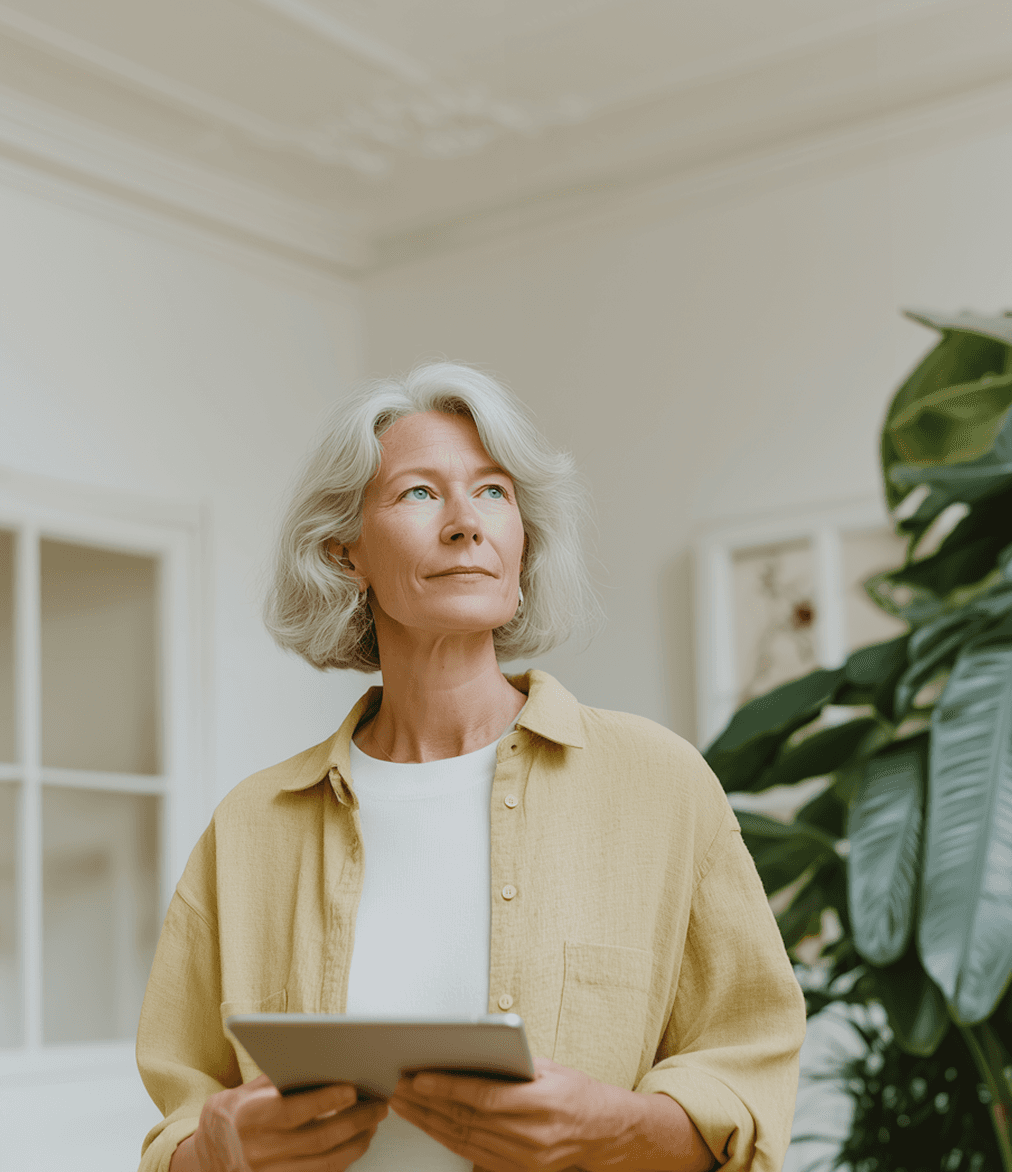 A peaceful senior woman in a neutral interior environment holding a tablet device.