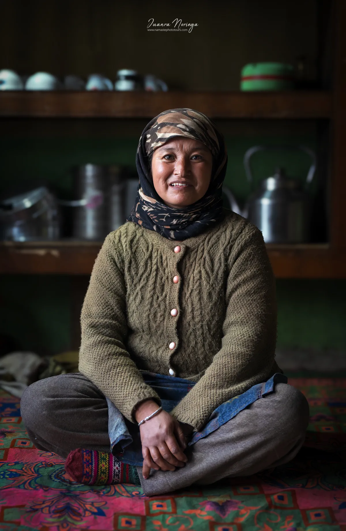 Mujer sonriente sentada en la cocina de una casa tradicional de Ladakh