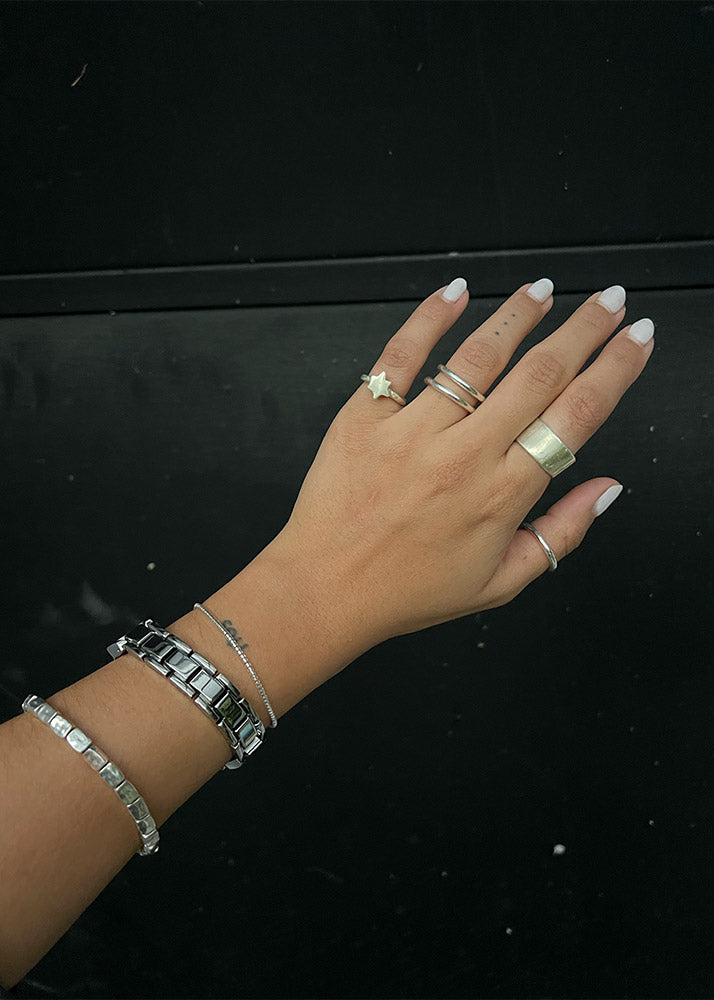 Hand with multiple silver rings and a bracelet on a black background