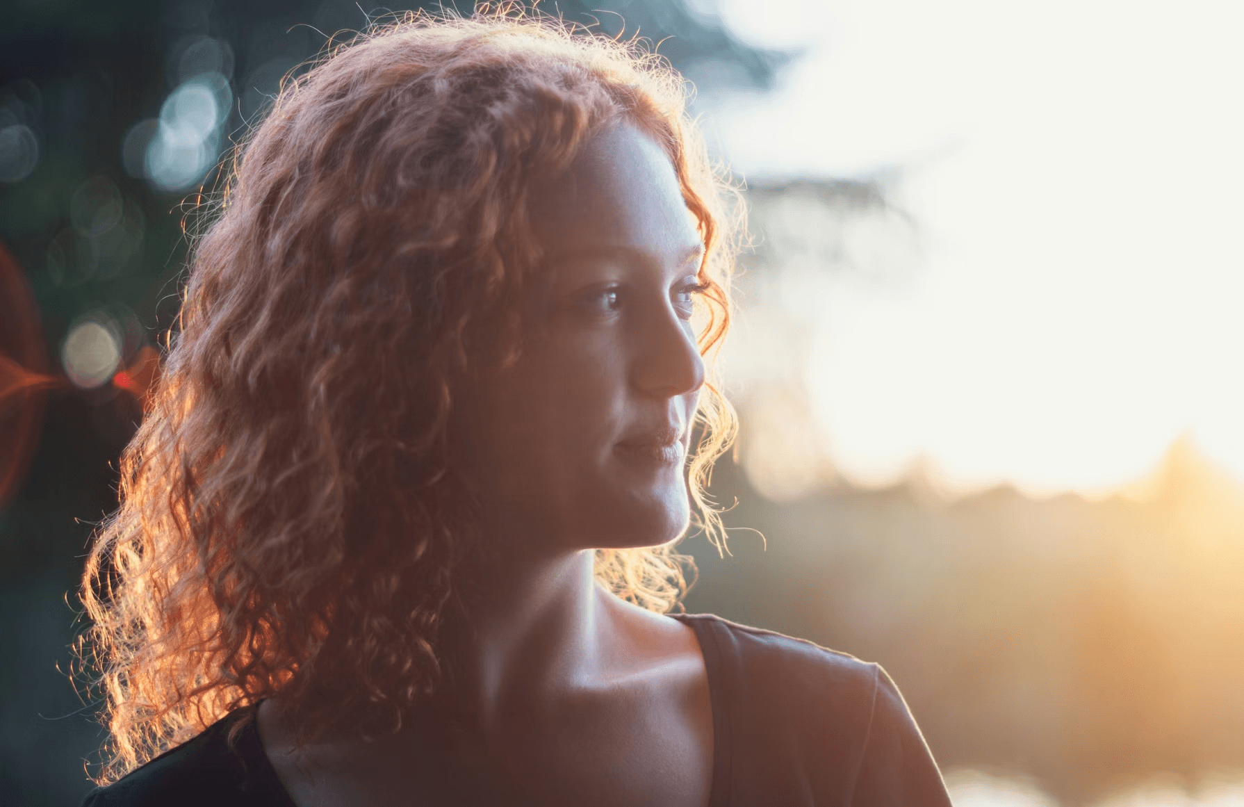 Young woman with curly red hair in sunlight