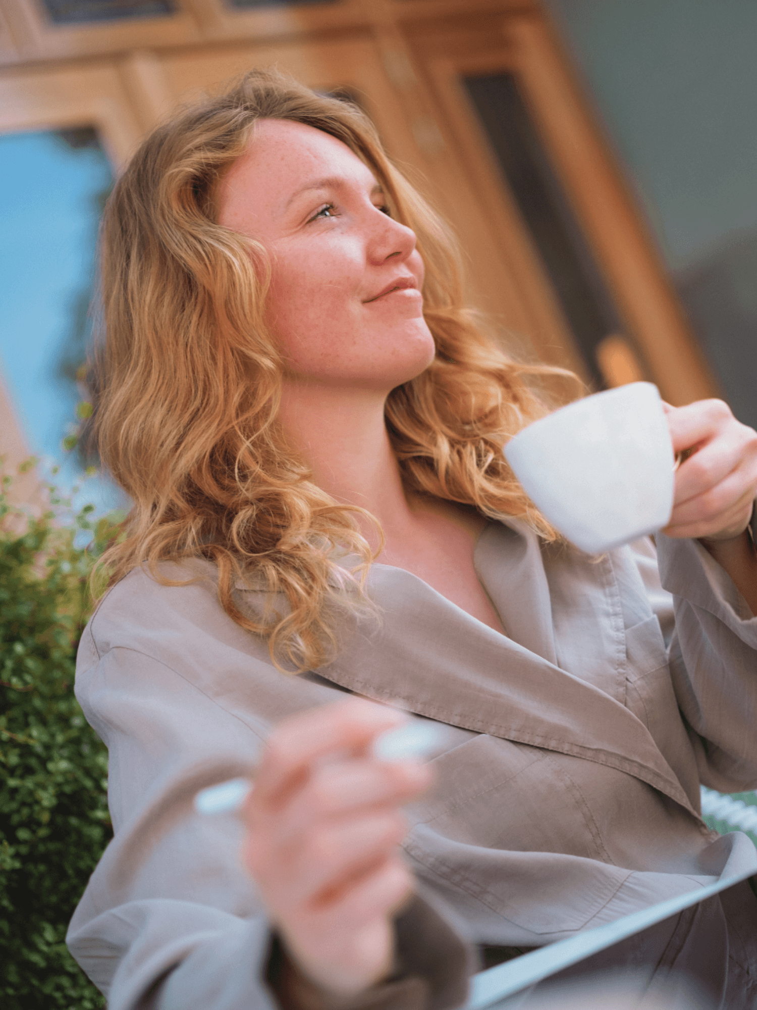 A smiling couple takes a selfie under a clear blue sky. The woman wears a red jacket, and the man, in a green top, holds a smartphone.