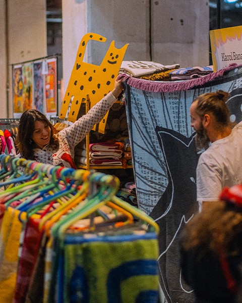 Zdjęcie przedstawiające dwie osoby pokazujące designerski koc na swoim stanowsiku targowym.